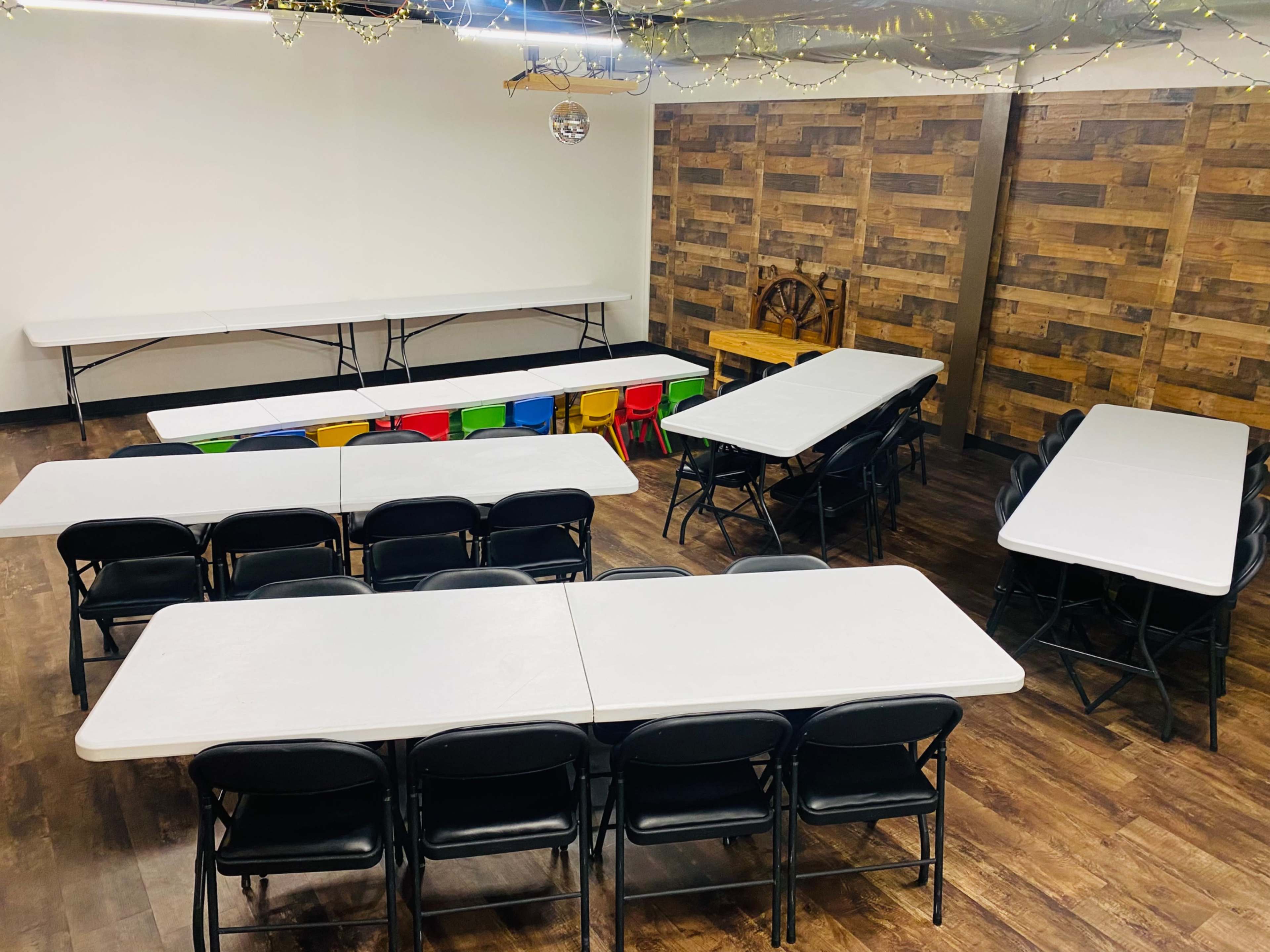 A room set up with multiple folding tables and chairs arranged in a layout against a wooden accent wall.