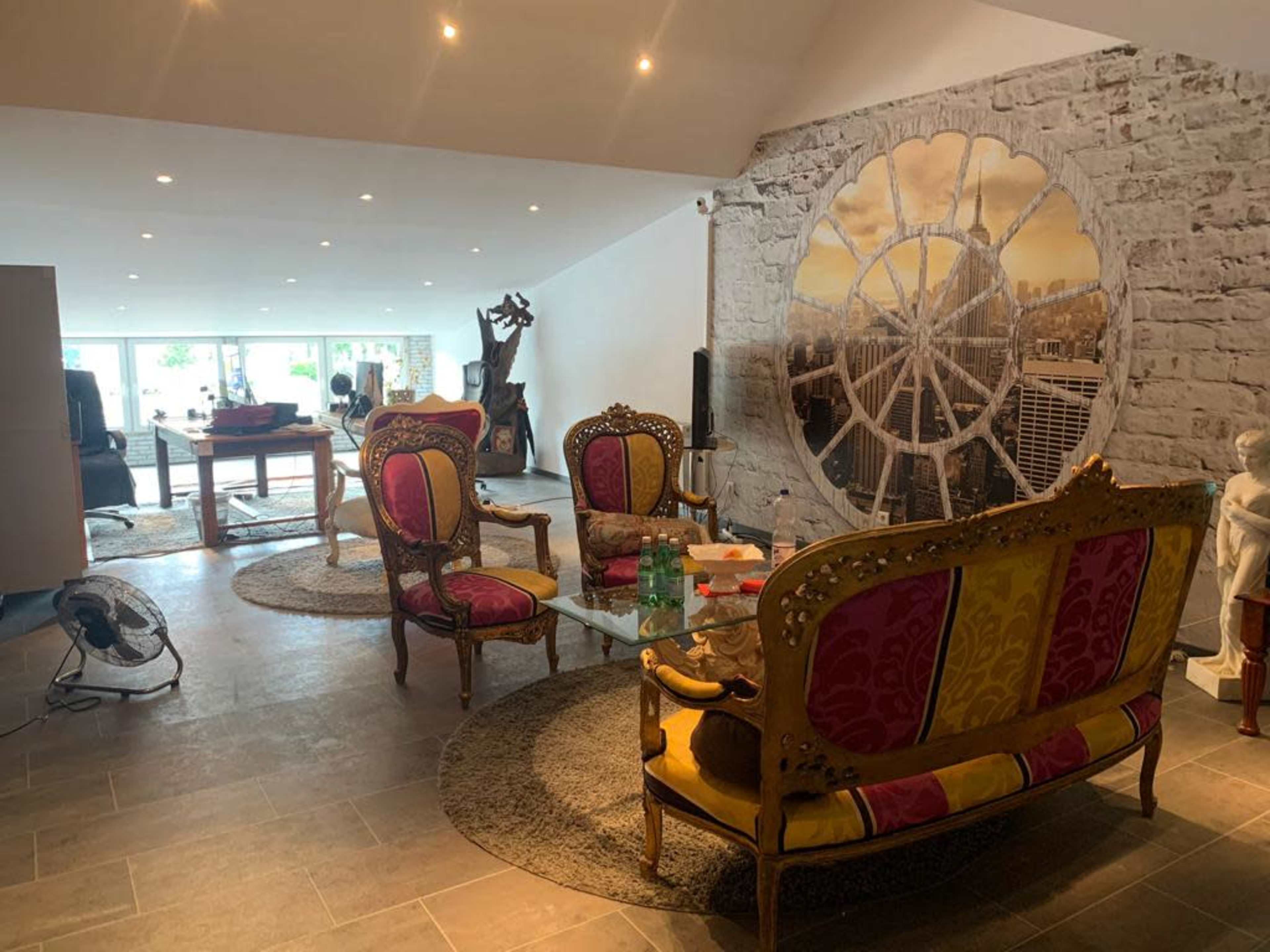 The room features elaborate, colorful chairs arranged around a glass table, with a large decorative mural and a stone wall as the backdrop.
