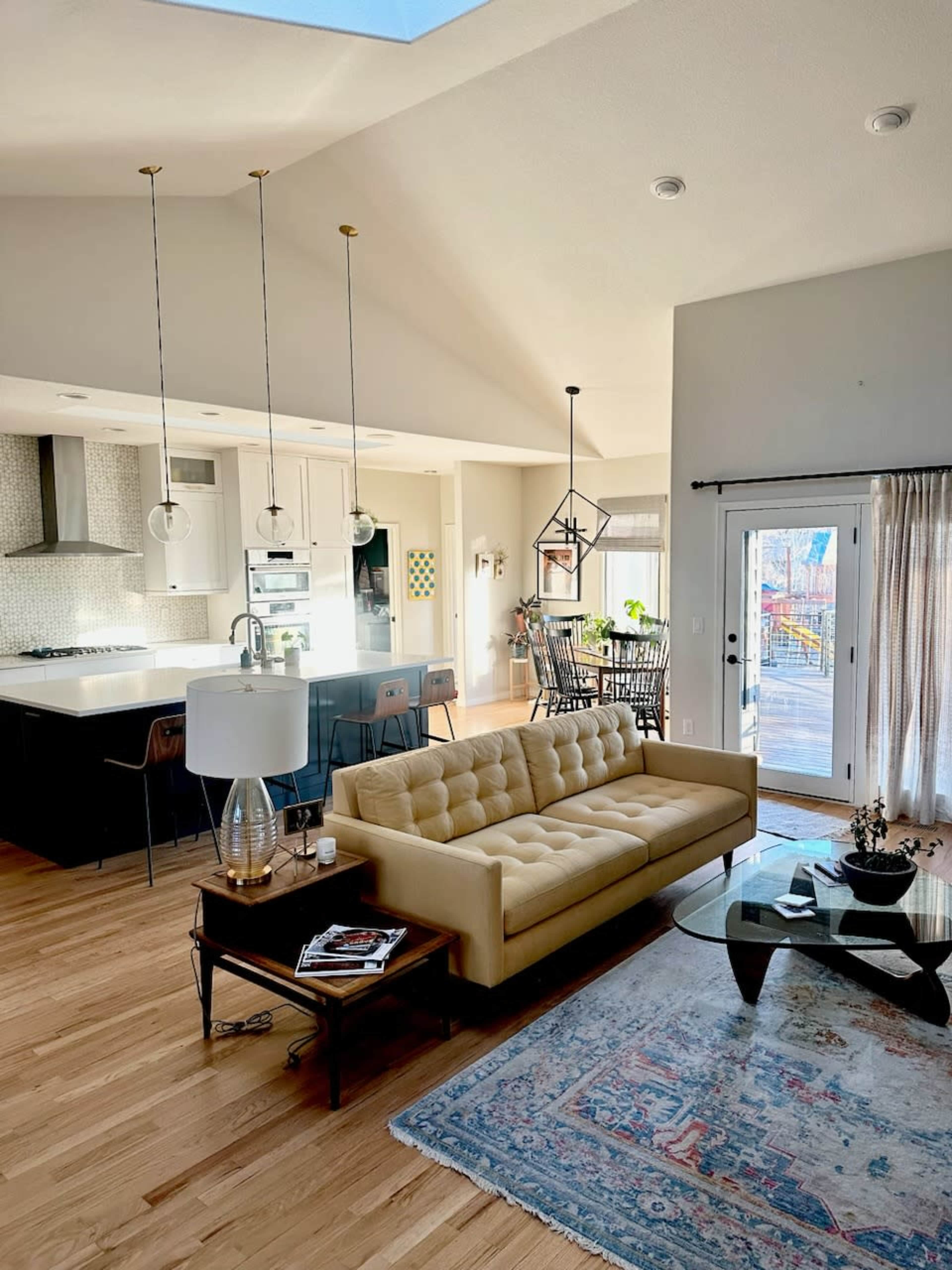 A modern living room with a beige tufted sofa, a coffee table, and an open kitchen area in the background.