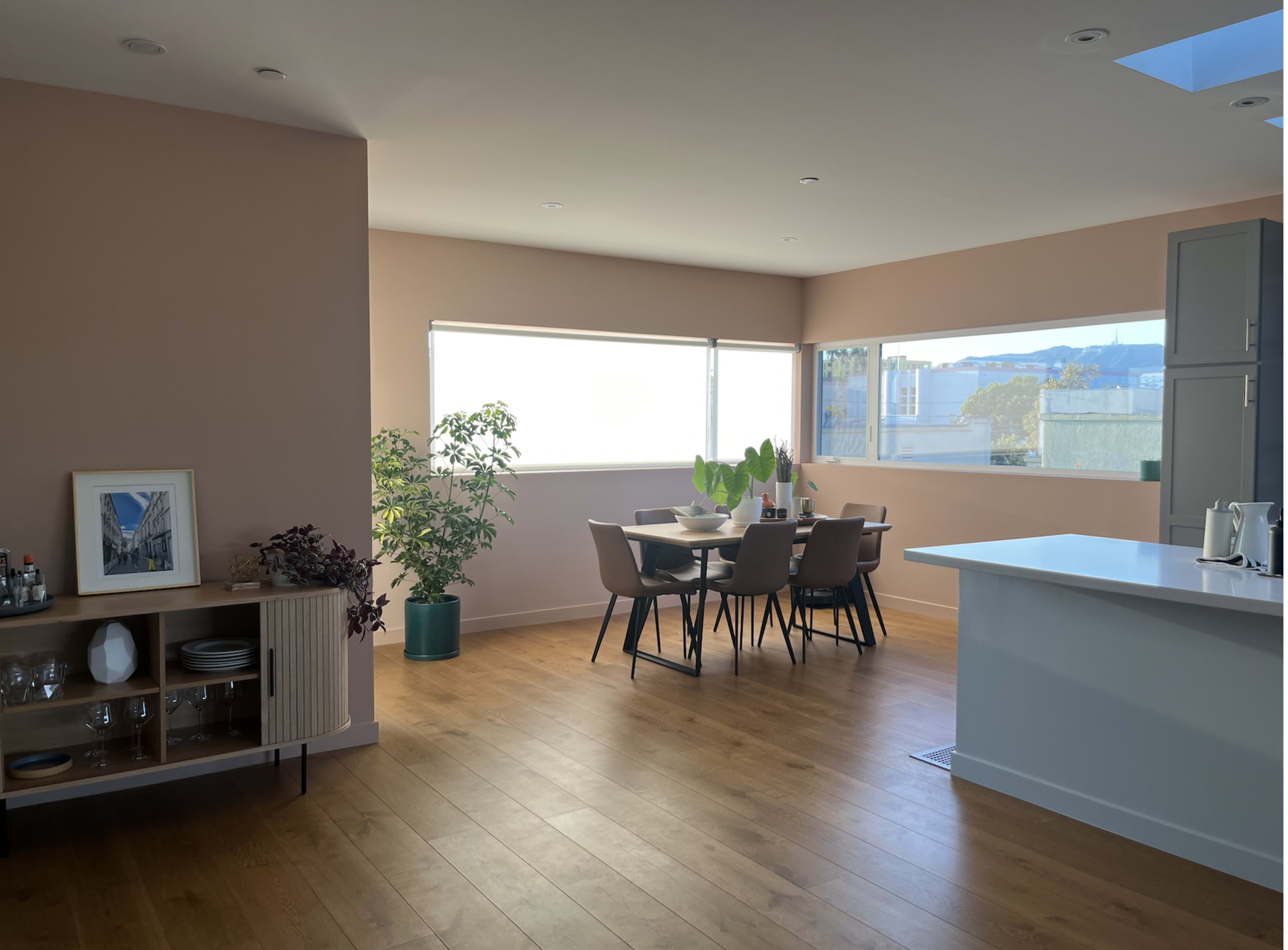 A modern, open-concept kitchen and dining area features a large window, a wooden dining table with chairs, and minimalistic decor.