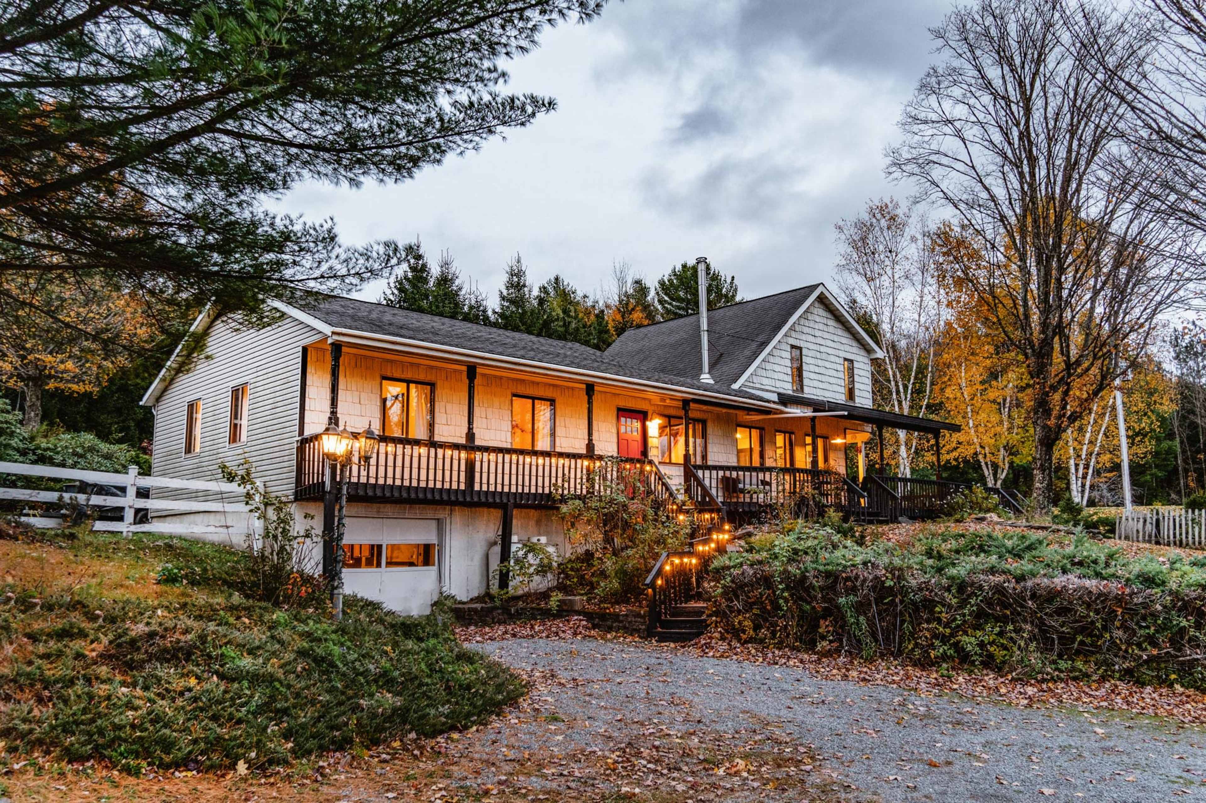A two-story house with a front porch and a driveway surrounded by trees and autumn foliage.