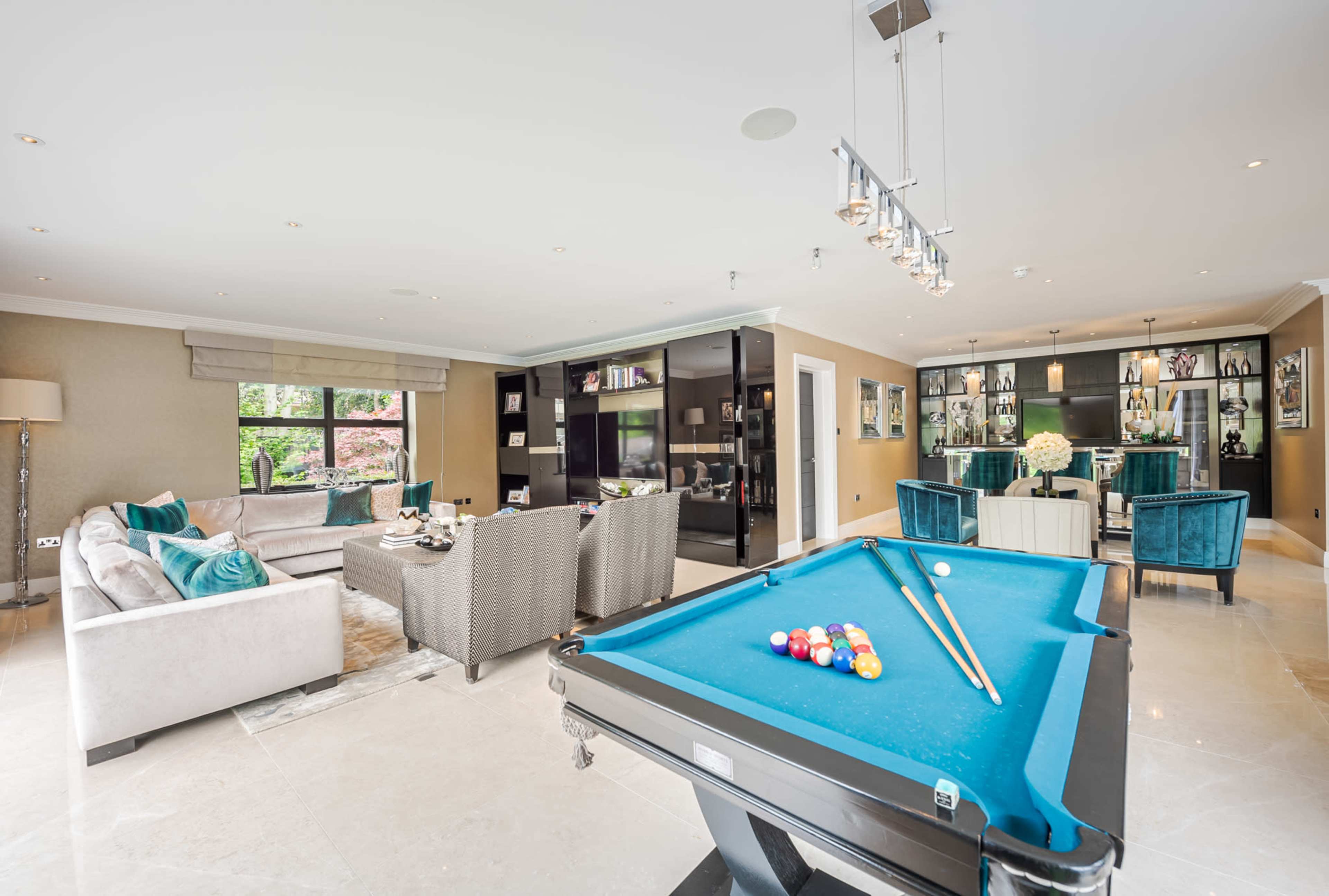 A modern living room featuring a billiards table in the foreground, a comfortable seating area, and a dining space with stylish furnishings in the background.