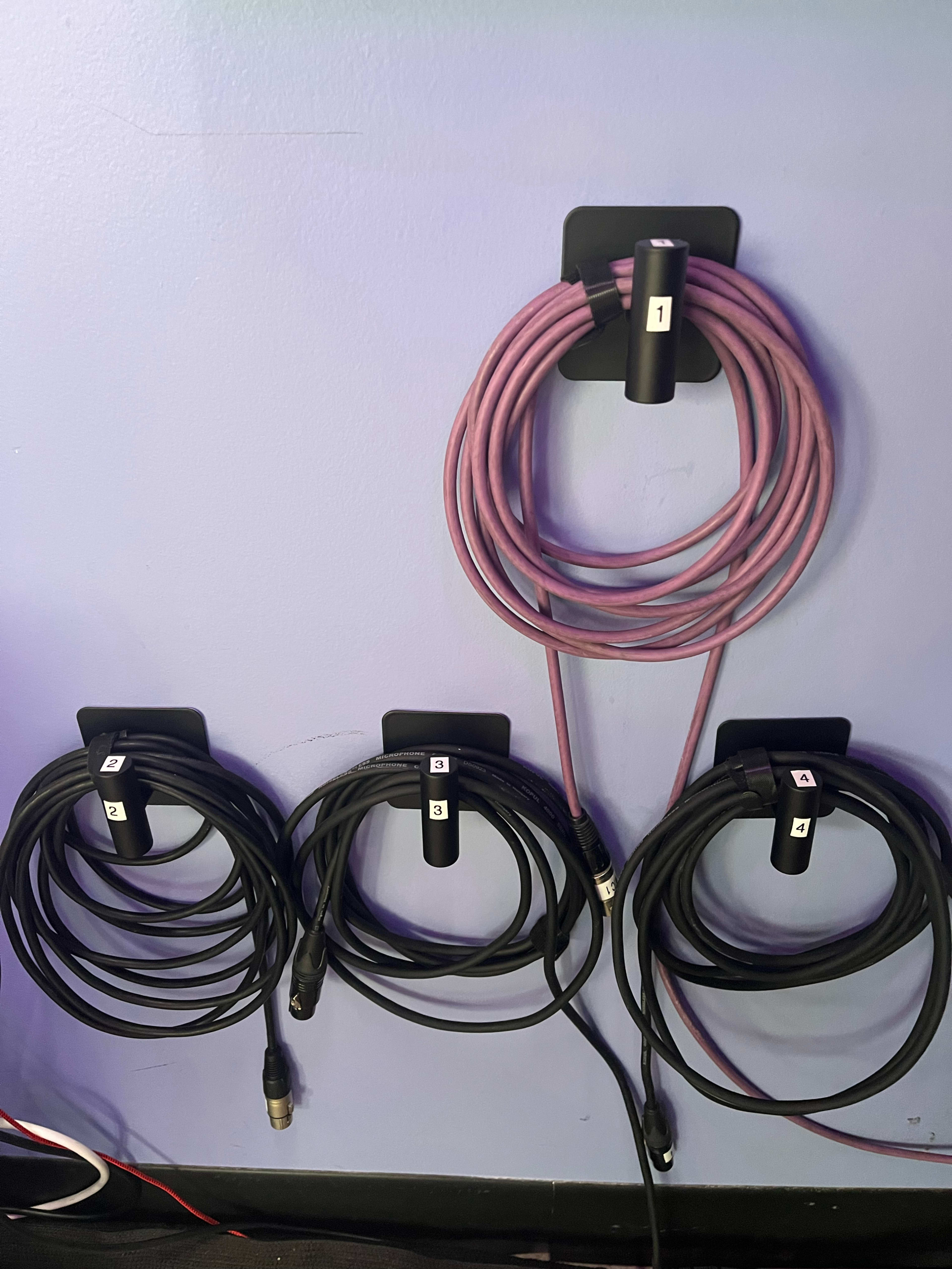 The image shows several audio cables organized and hung on wall-mounted clips, with two purple and three black cables labeled numerically.