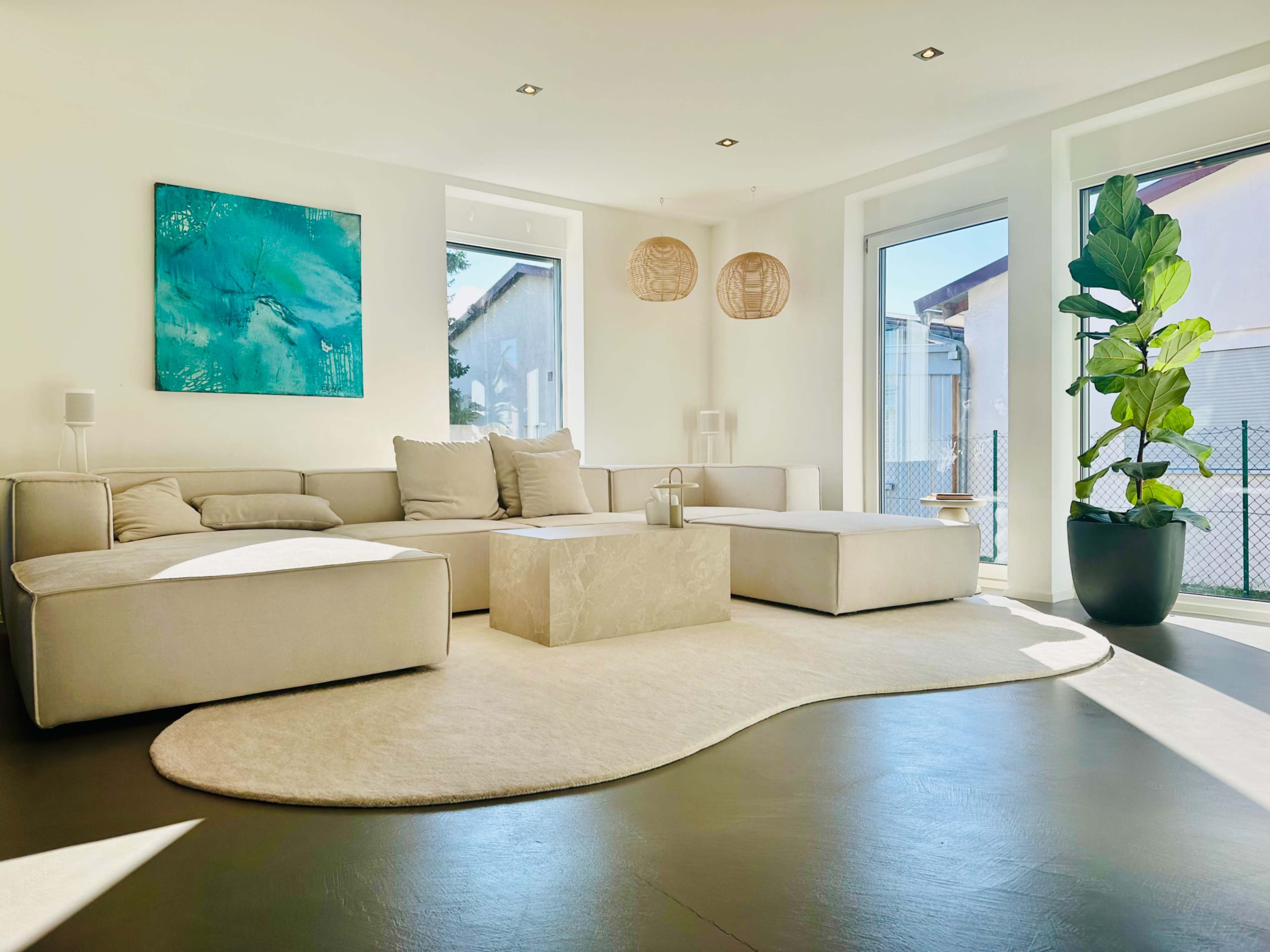 The living room features a modern, sectional sofa, a coffee table, and large windows allowing natural light to fill the space.