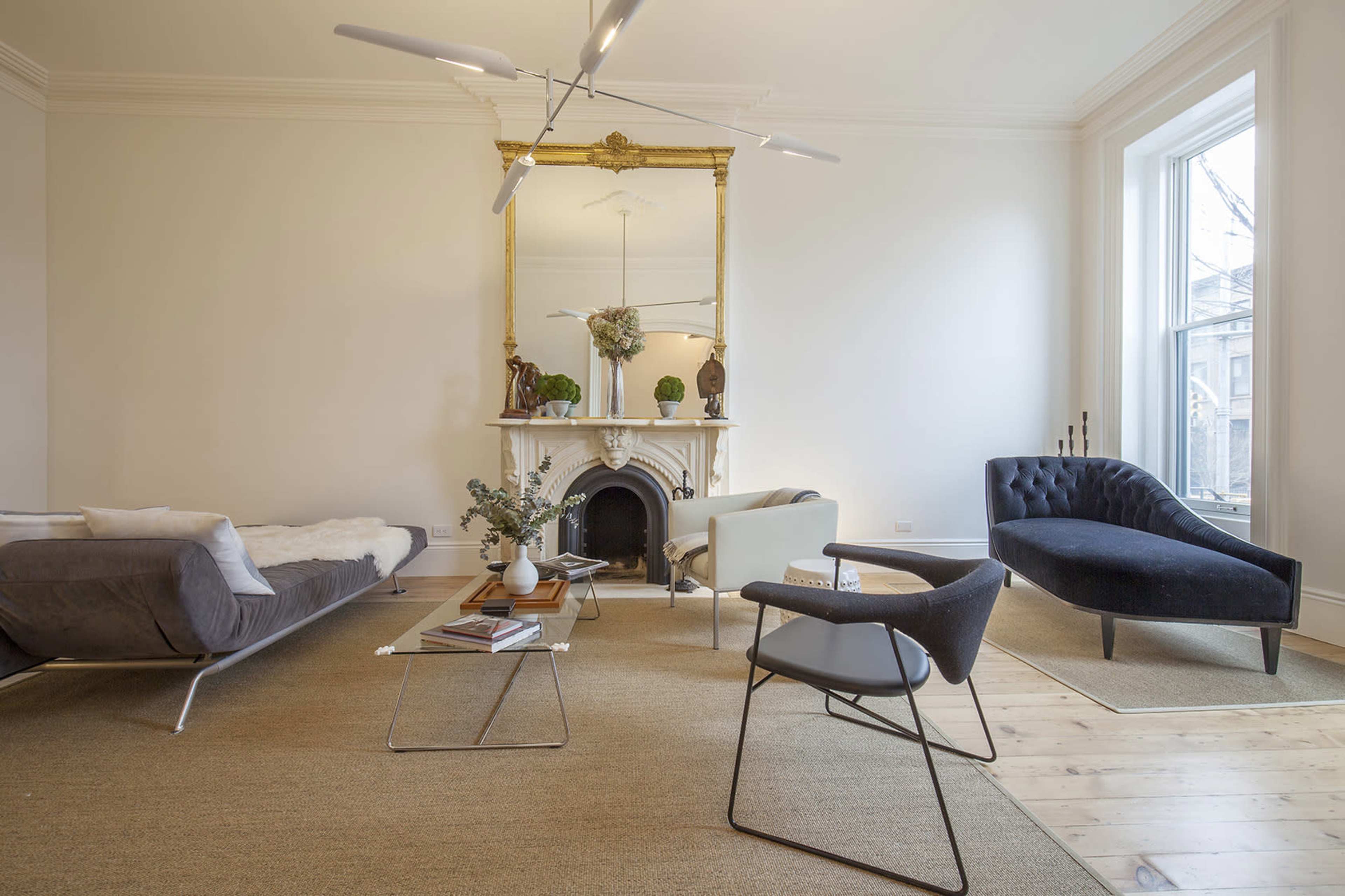 The image shows a modern living room with a minimalist design, featuring a chaise lounge, a sofa, and a fireplace with a large mirror above it.