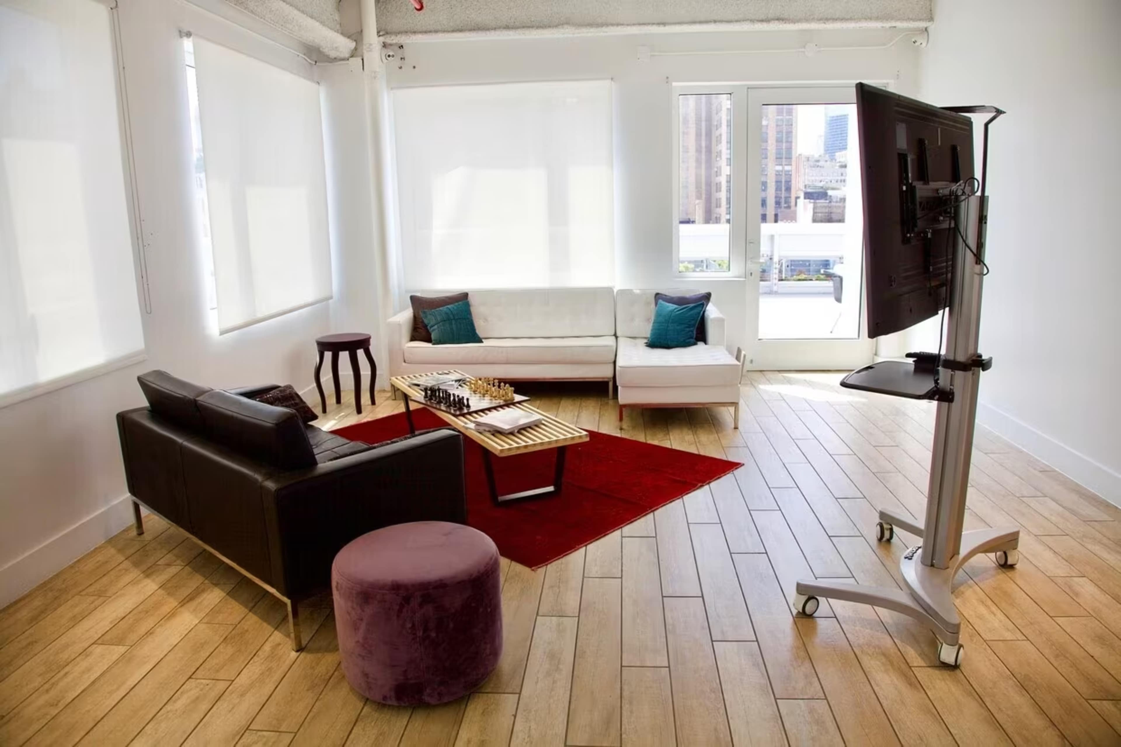 A minimalist living space with two sofas, a coffee table, a small side table, and a TV mounted on a stand, all set against a backdrop of large windows.