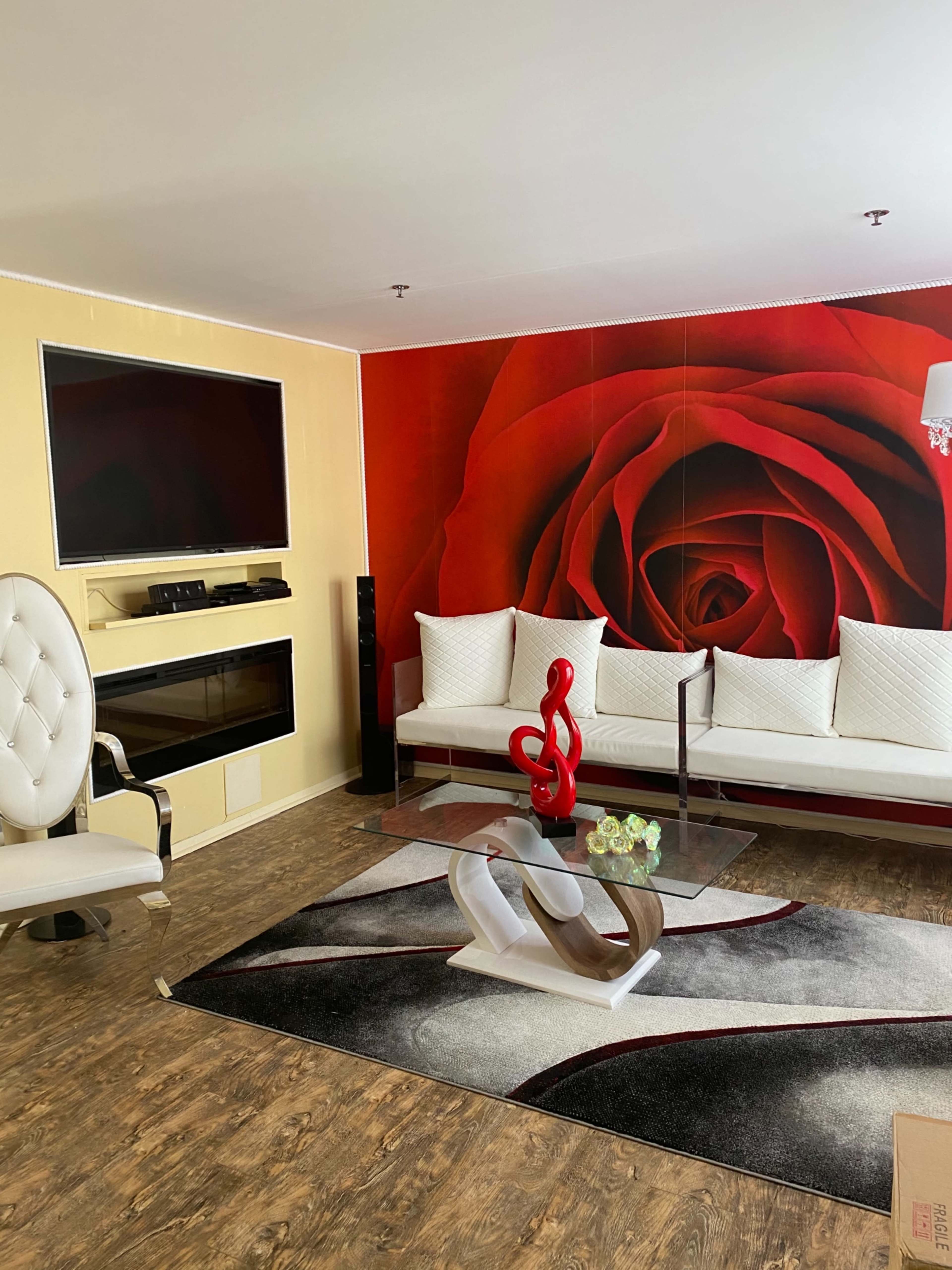 The living room features a large red rose mural on one wall, a white sofa with decorative pillows, a sleek glass coffee table, and an armchair beside a flat-screen TV.