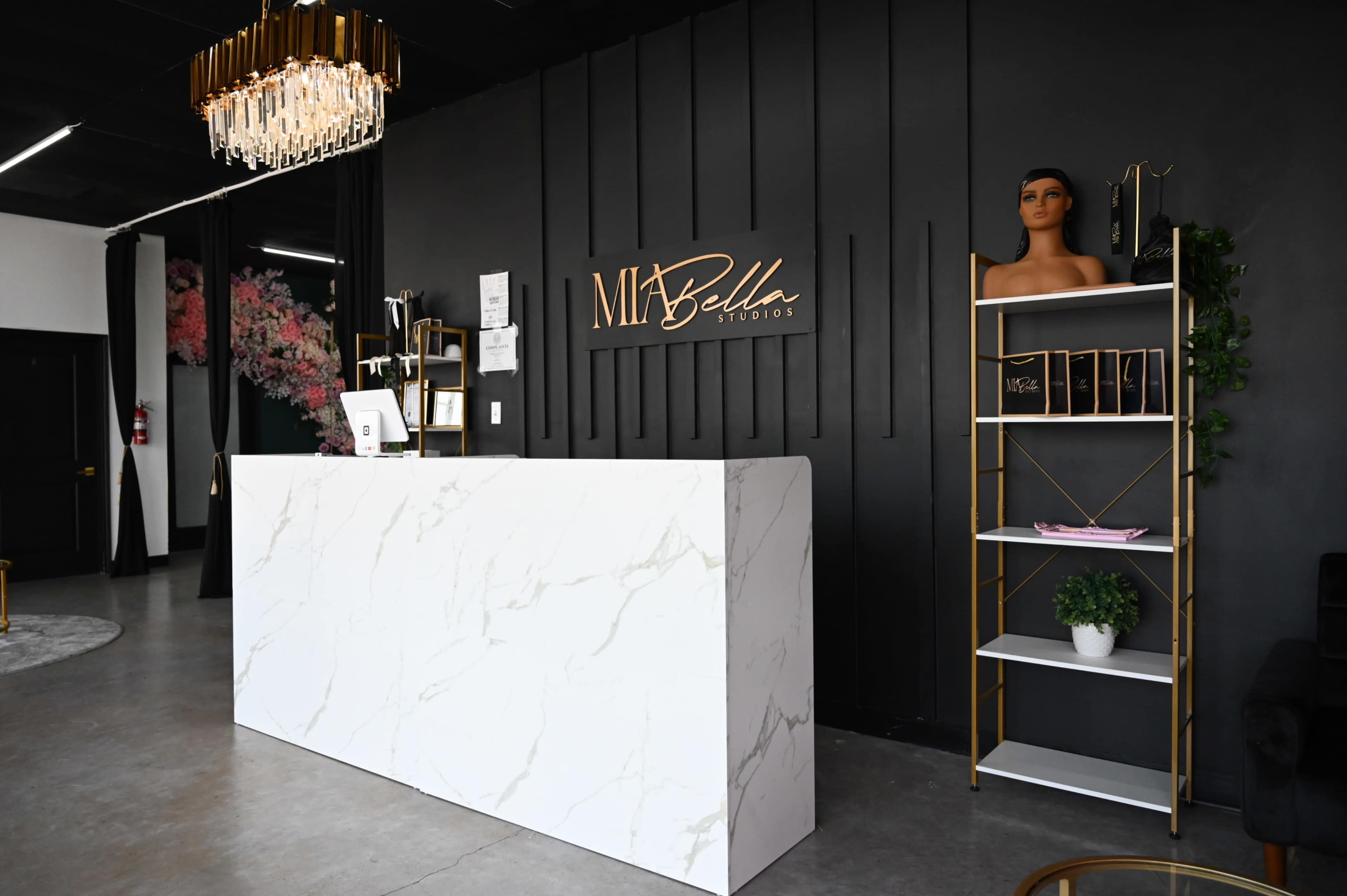 A modern reception area with a white marble counter, black walls, a chandelier, and a stylish shelving unit.