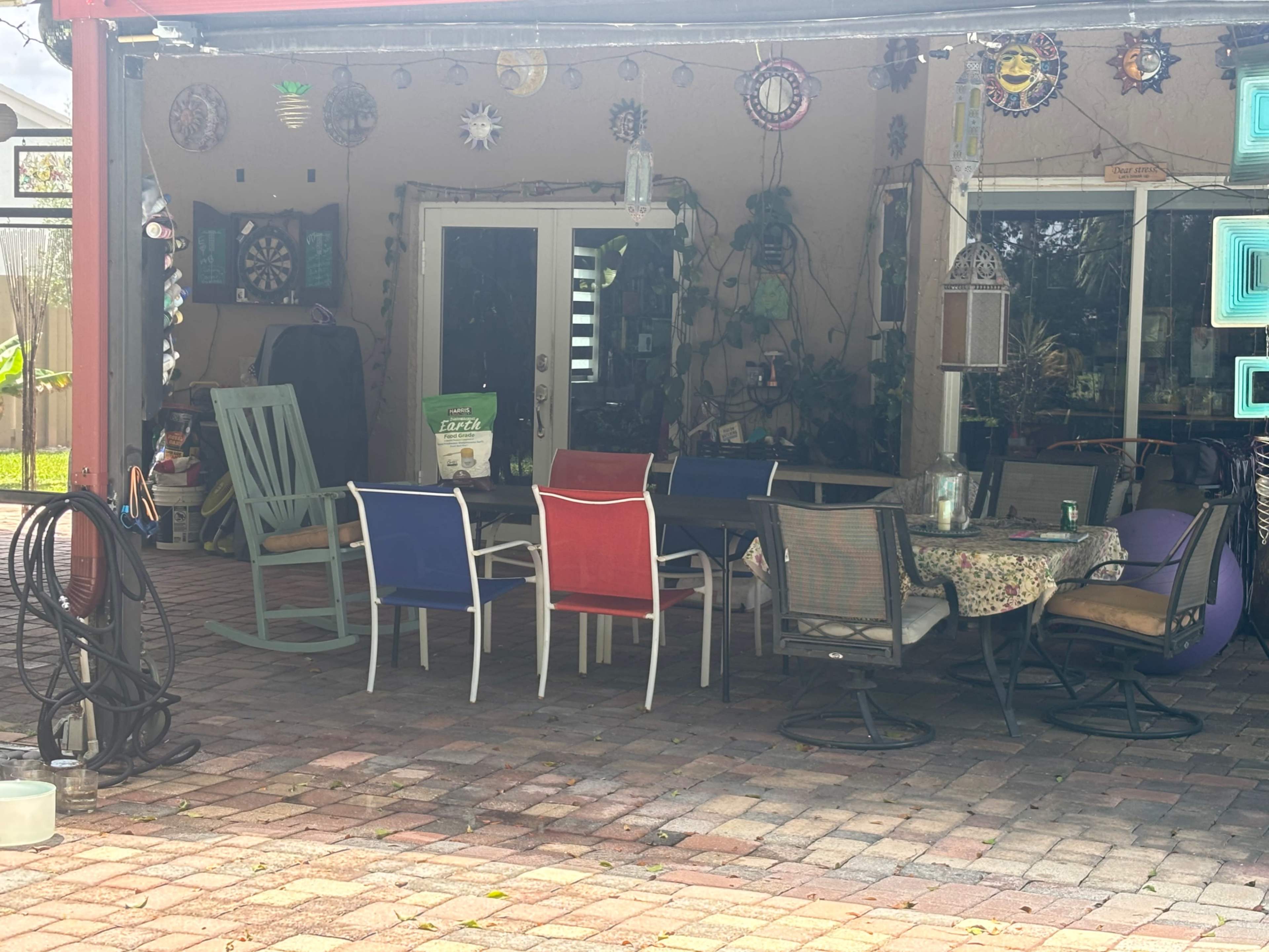 The image shows a patio area with various chairs, a table, and decorative items hanging on the walls.