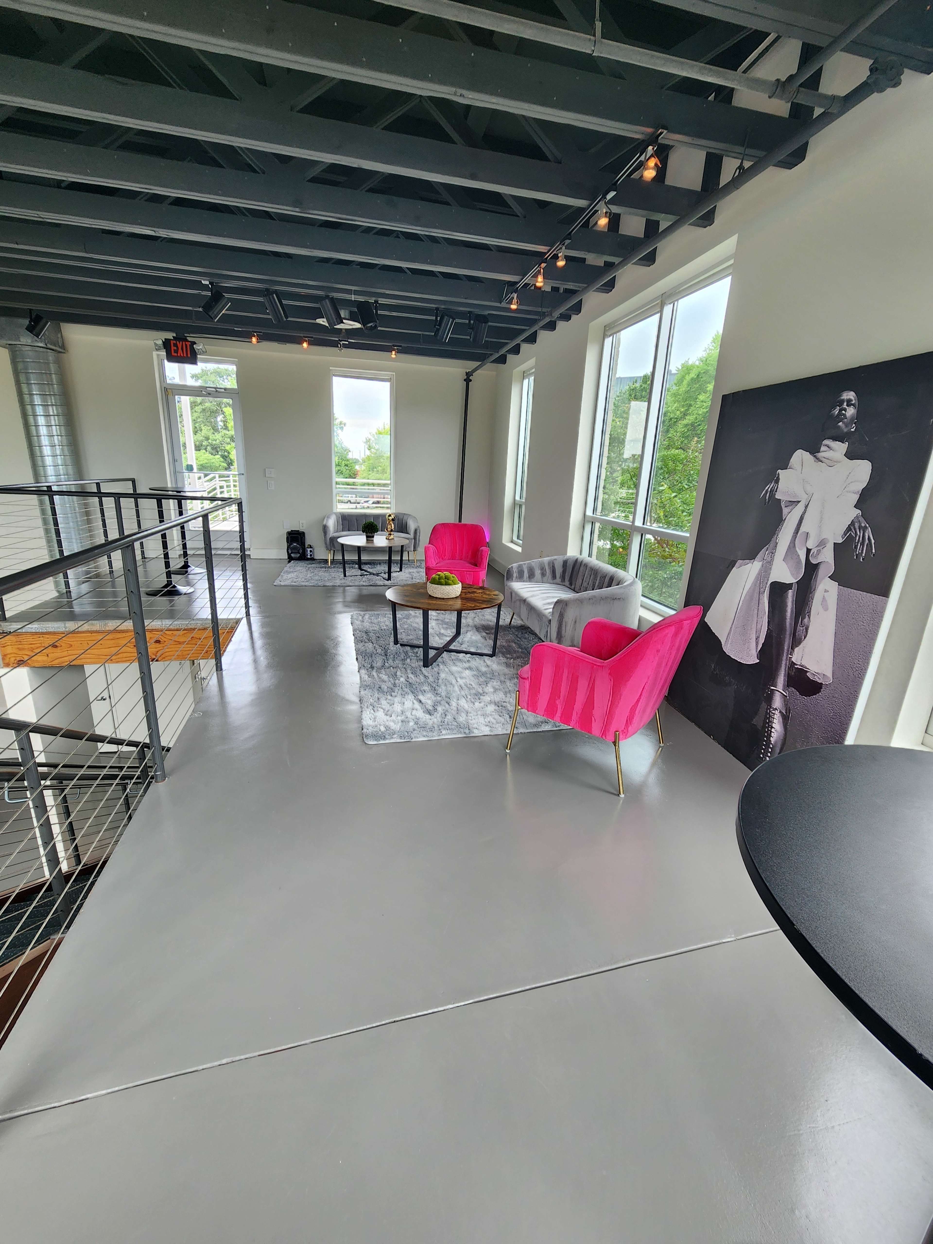 The spacious interior features pink upholstered chairs, a gray sofa, and a large black-and-white artwork against the wall, with plenty of natural light coming through large windows.