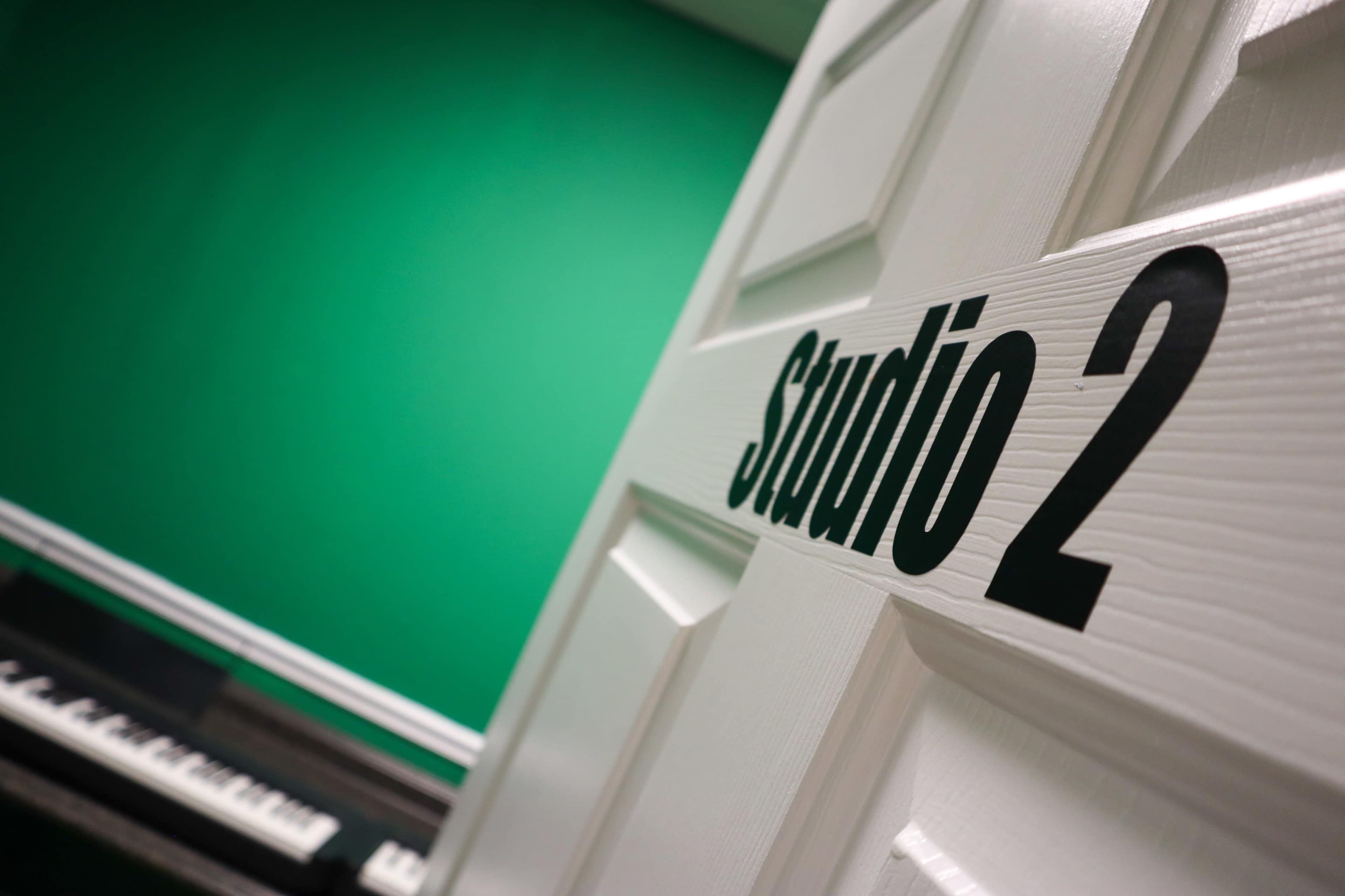 A white door labeled "Studio 2" is partially open in front of a vibrant green wall with a keyboard visible in the background.
