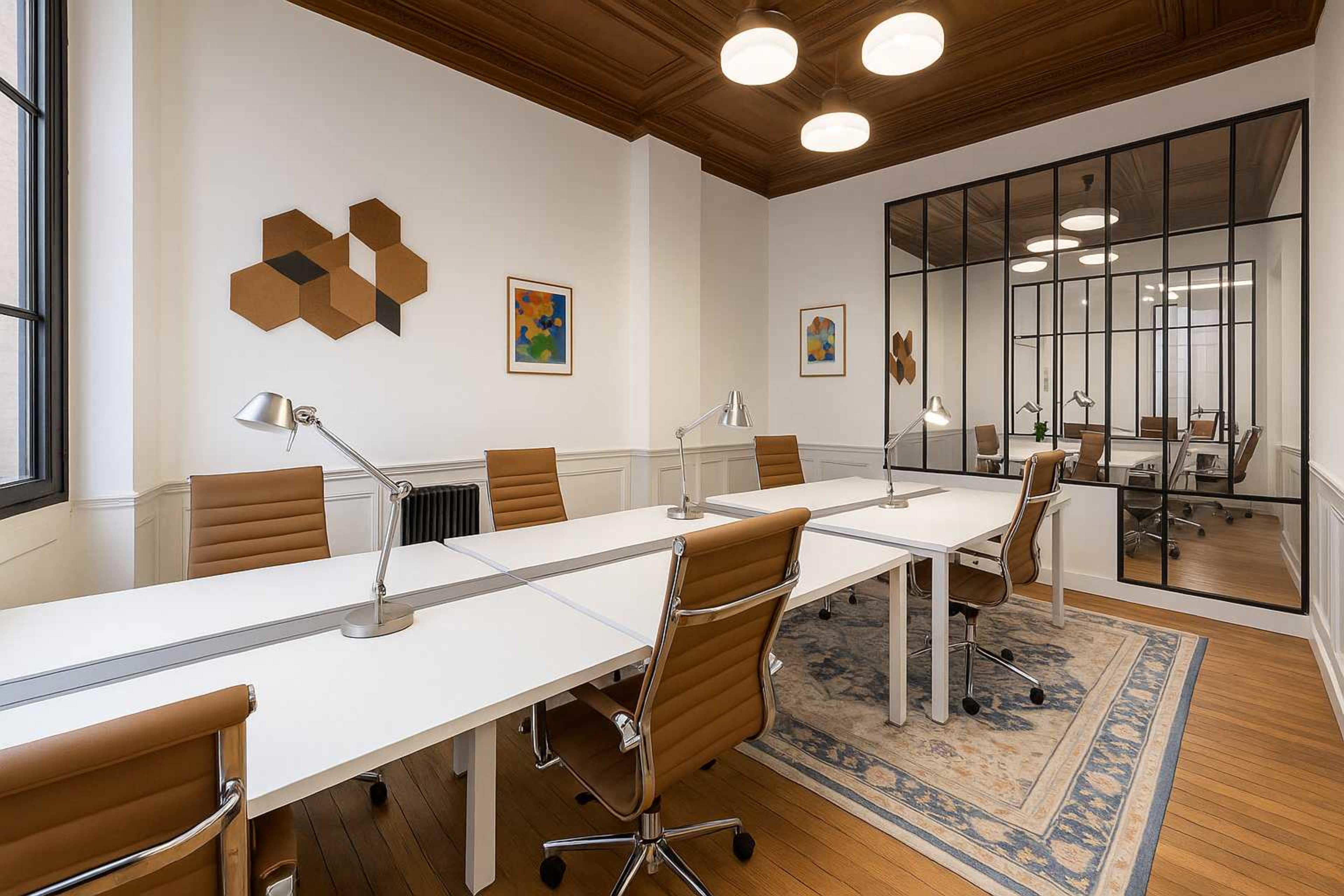 The image shows a modern conference room with a long white table surrounded by brown leather chairs, complemented by artwork on the walls and a glass partition leading to another workspace.
