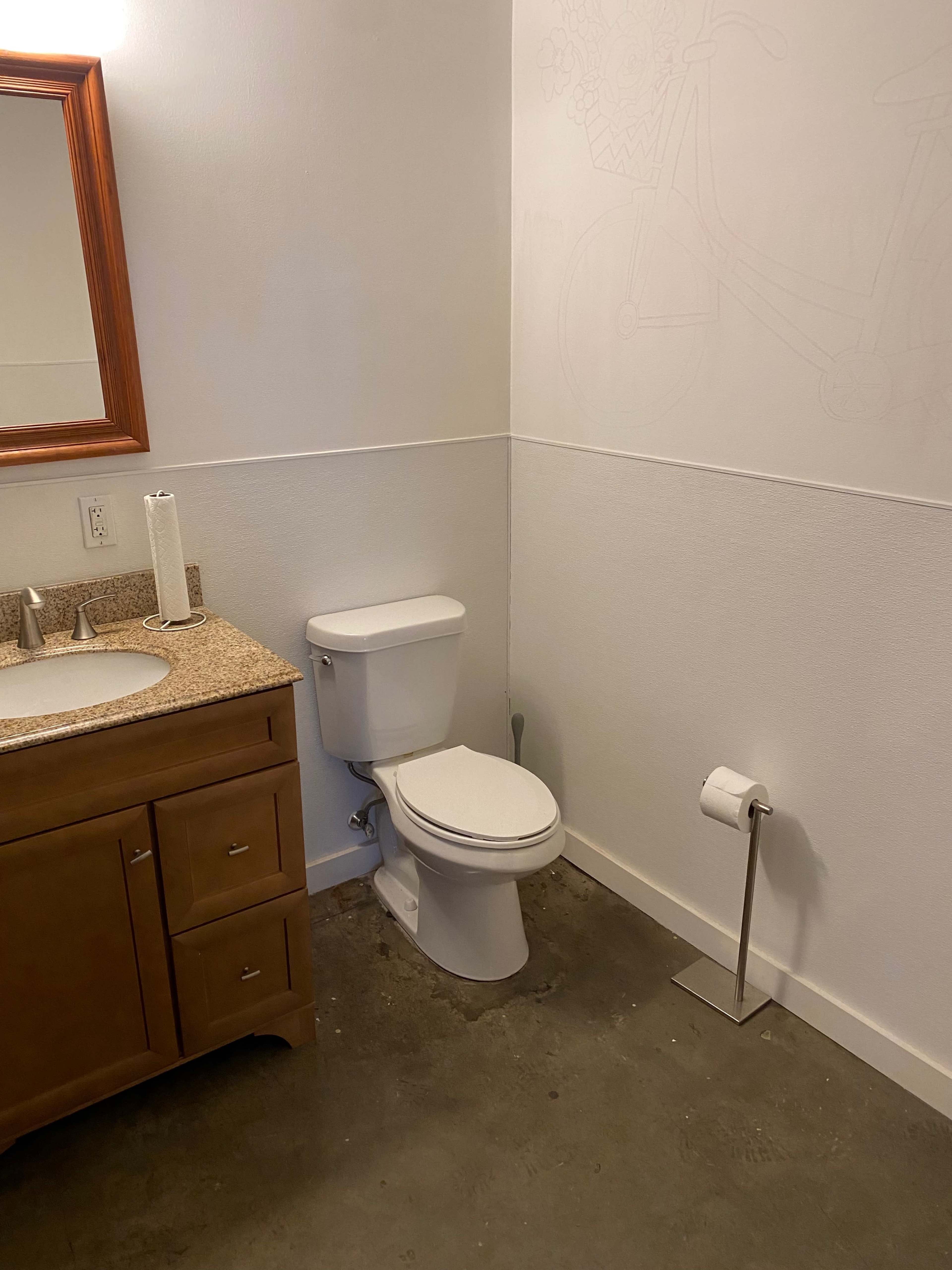 A small bathroom featuring a toilet, a sink with a granite countertop, a mirror, and a paper towel dispenser.