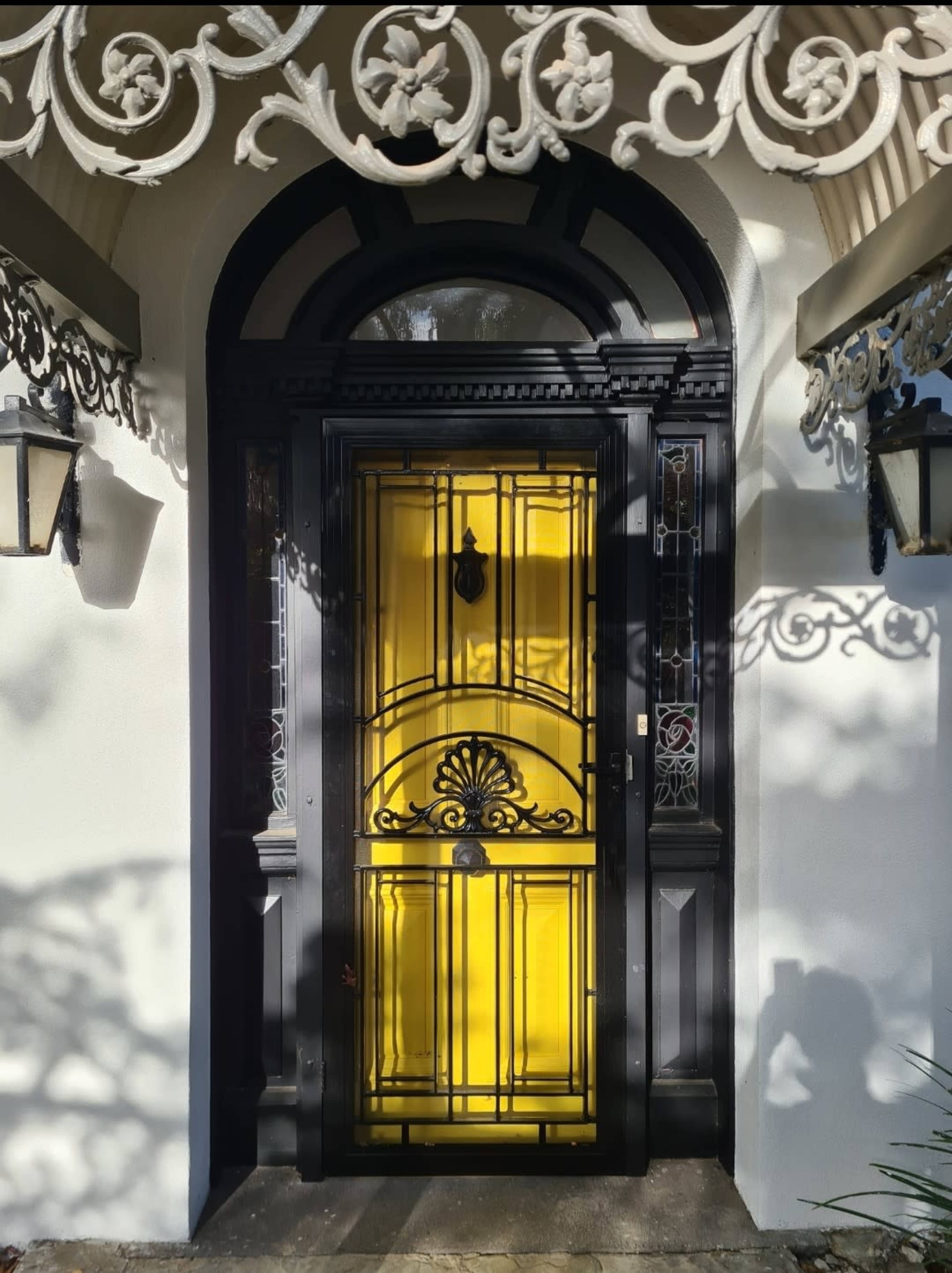 A black and yellow ornate front door framed by intricate white decorative elements and two lanterns on either side.
