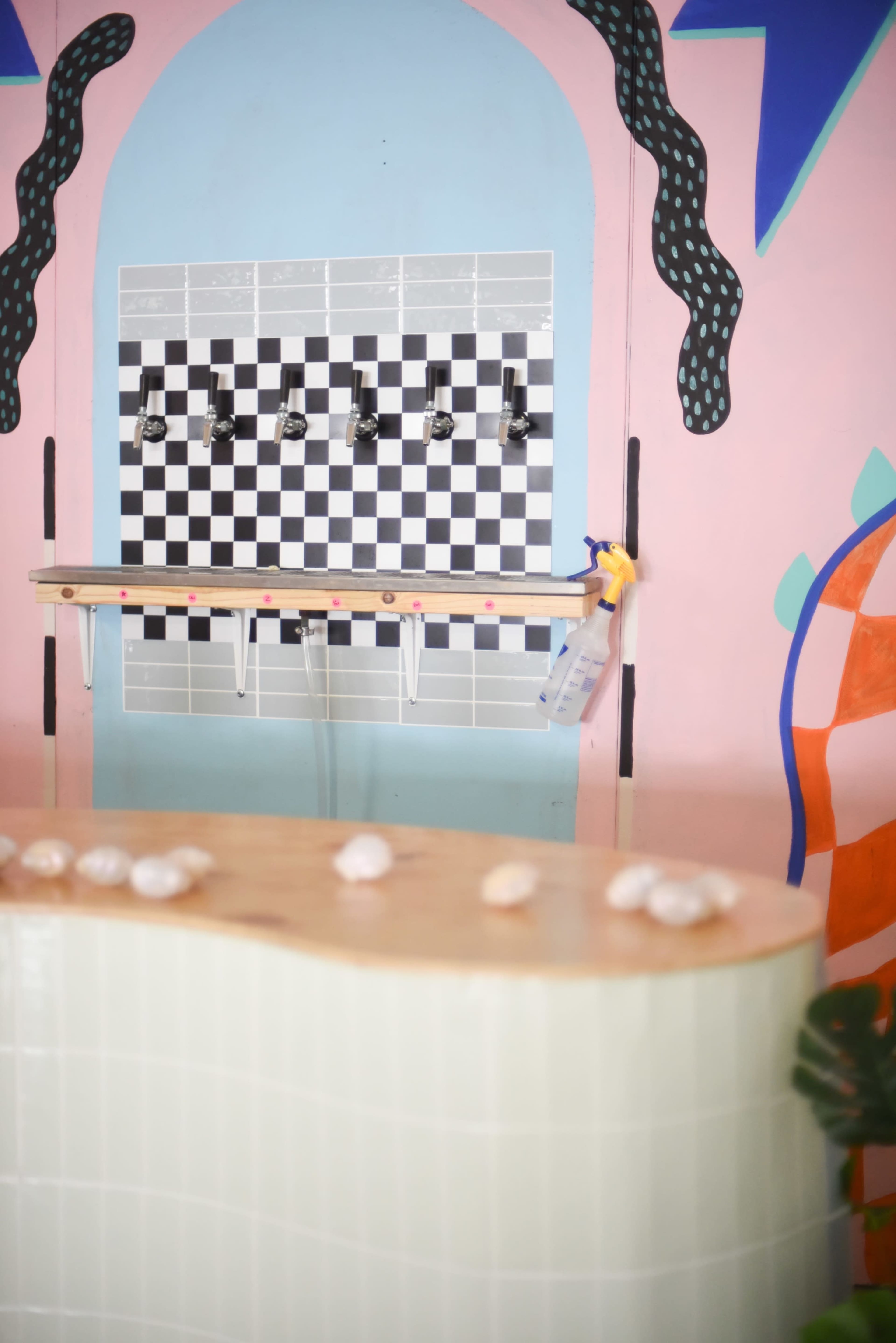 A colorful interior with a checkered wall and multiple faucets above a light-colored curved counter.