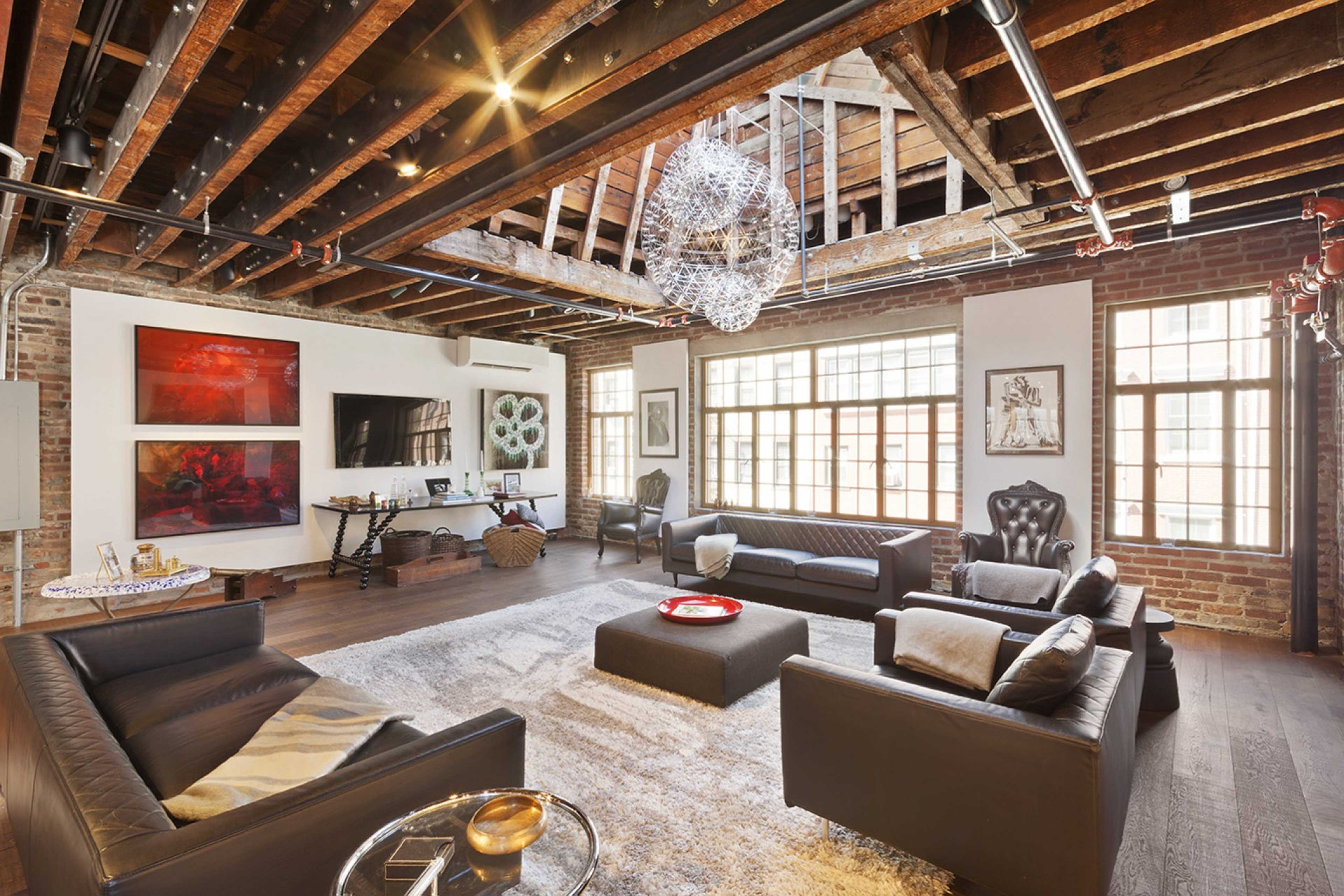 A spacious living room features exposed wooden beams, large windows, and modern furniture arranged around a central coffee table.