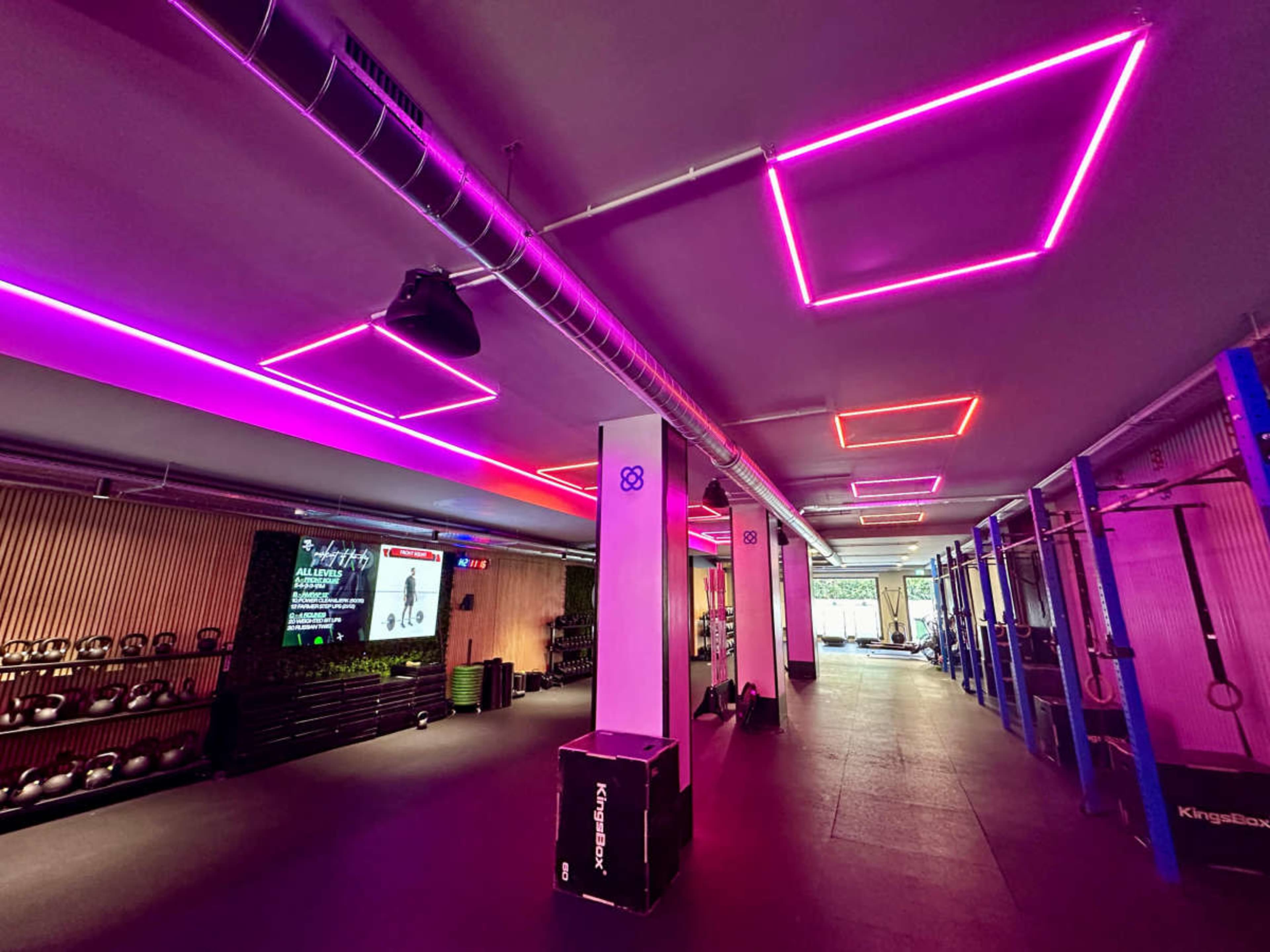 A gym interior featuring colorful LED lighting, exercise equipment, and an area for workout activities.