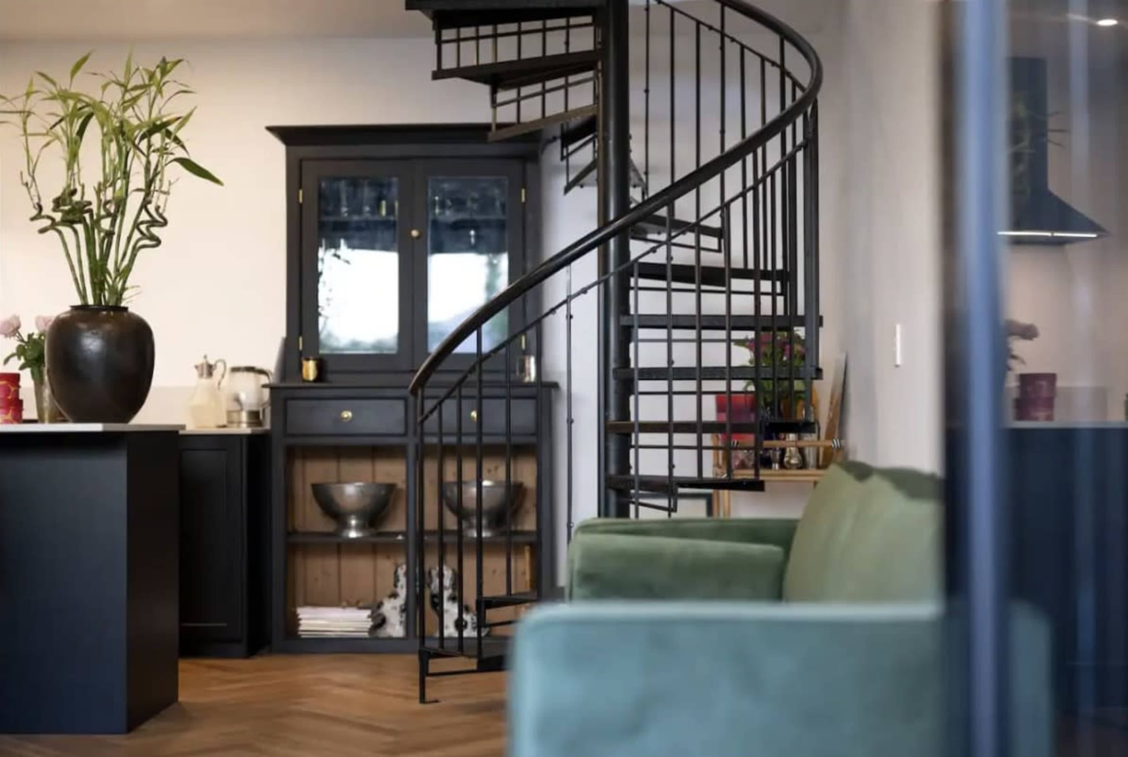 A spiral staircase leading to an upper level, with a black cabinet and a green sofa visible in a modern interior space.