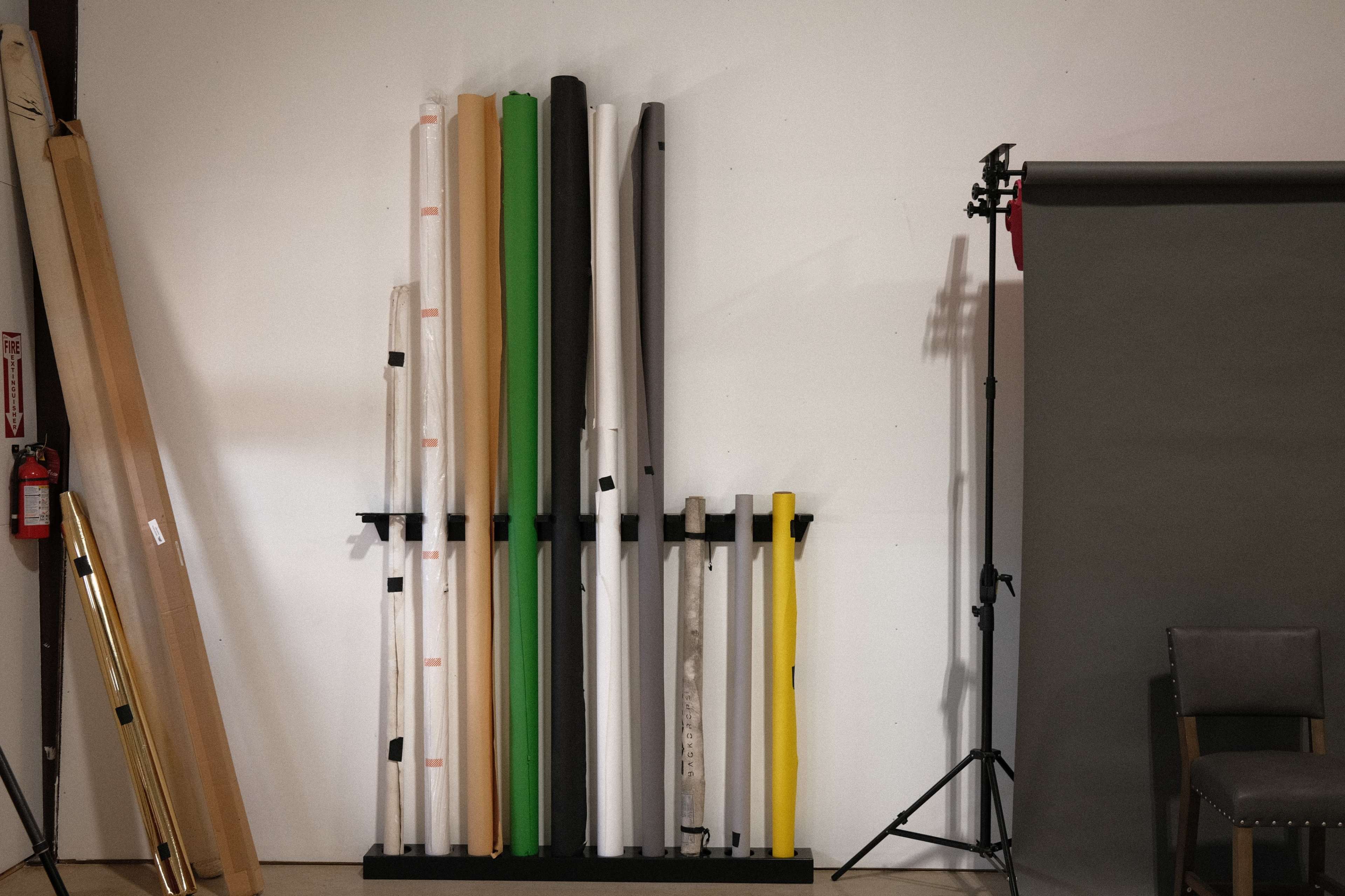 A collection of rolls of paper and backdrop materials is organized vertically against a wall, with a chair and backdrop support in the frame.
