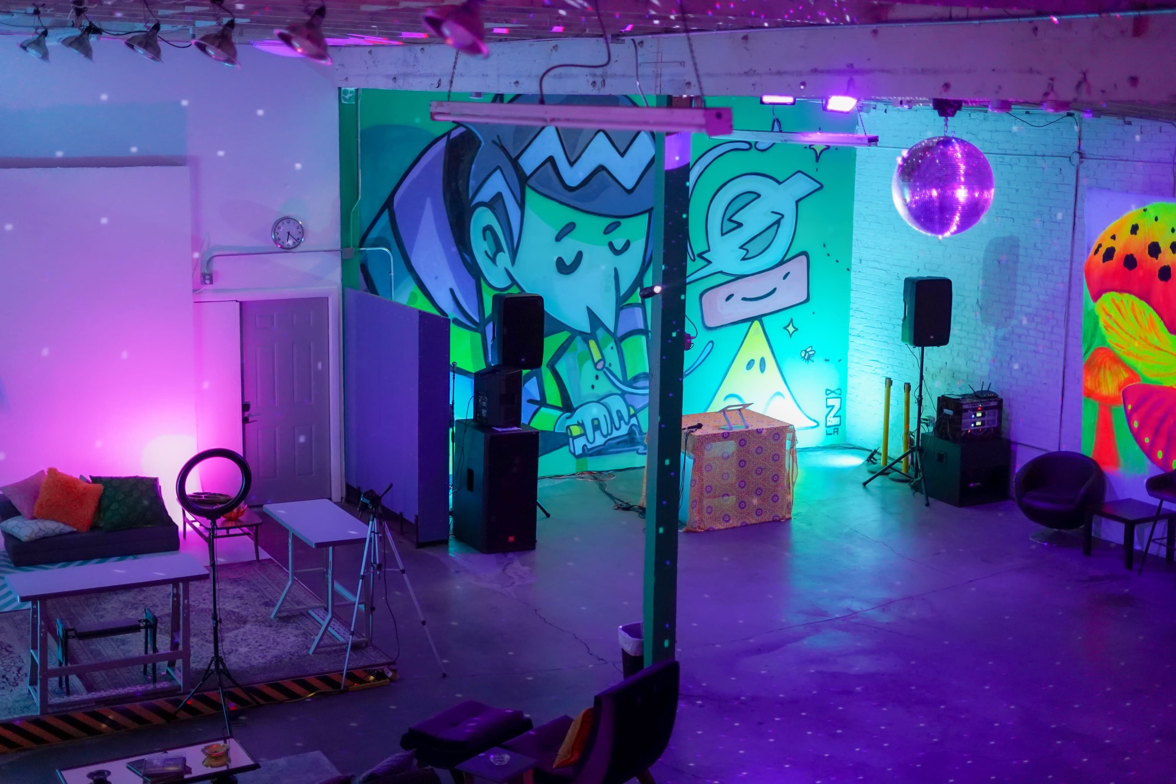 The image shows a vibrant indoor event space with colorful murals, a disco ball, and lounge seating arranged for a gathering.