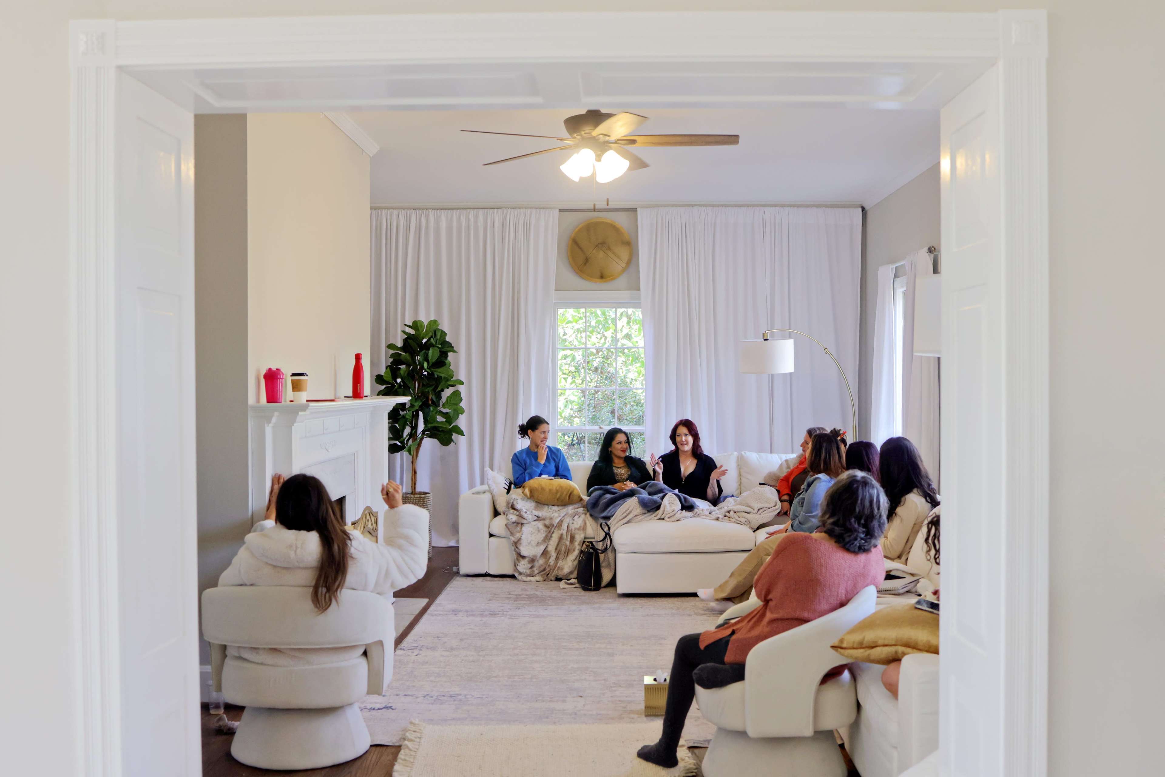A group of people sits in a light-filled living room on comfortable chairs and sofas.