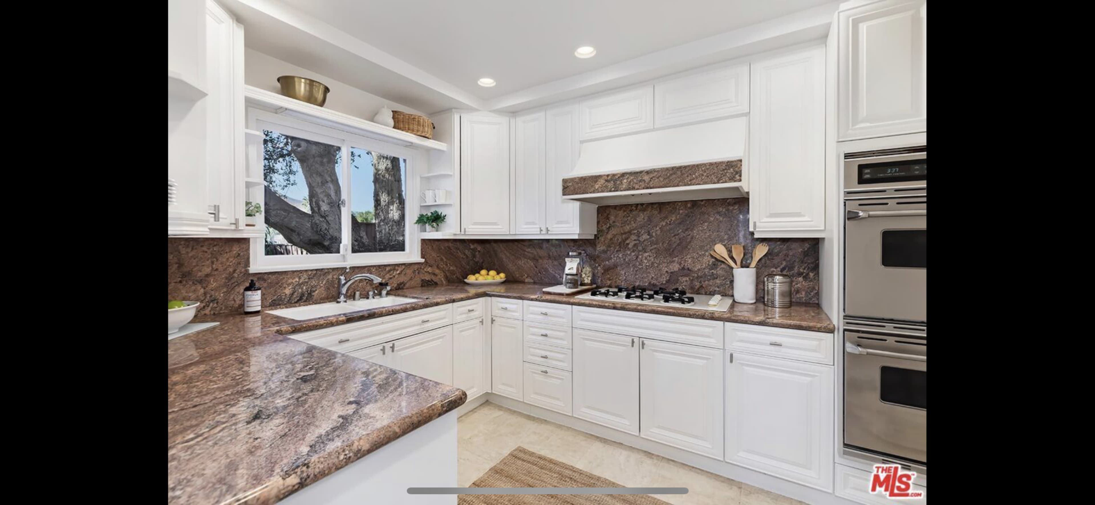 The kitchen features white cabinetry, a brown marble countertop, and stainless steel appliances, with a window overlooking an outdoor area.