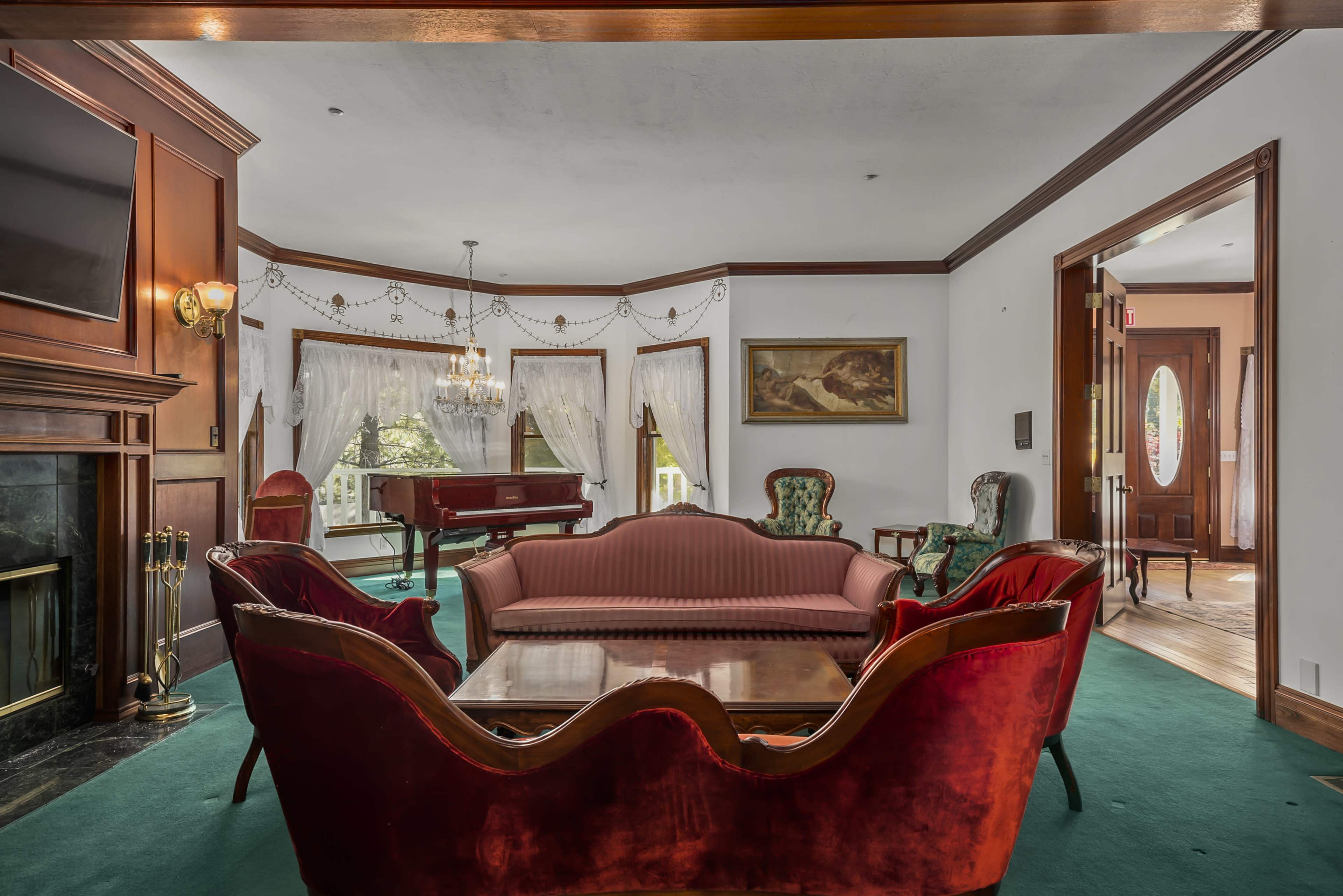 The scene features a living room with a red velvet sofa, two upholstered chairs, a glass coffee table, and a grand piano in the background.