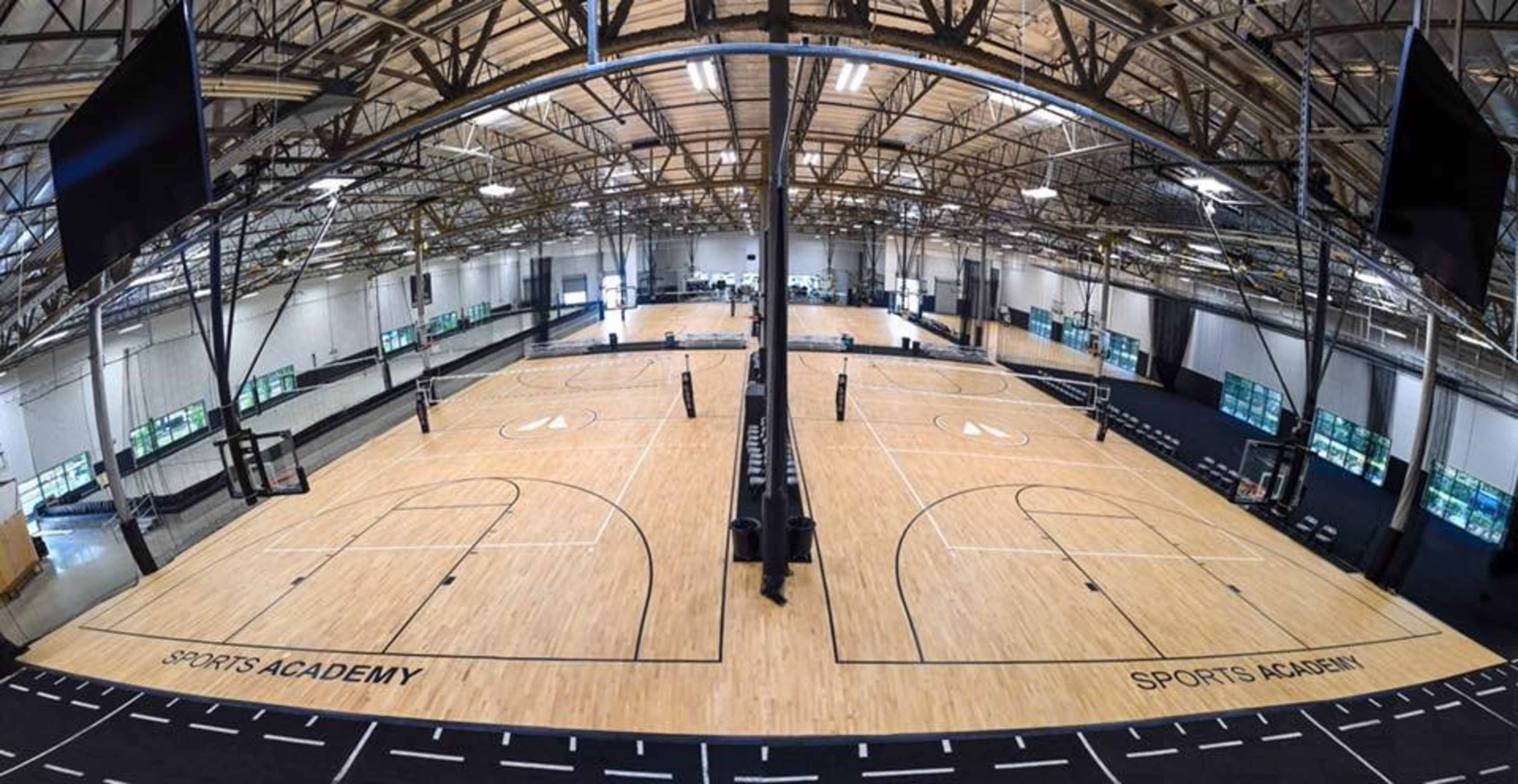 A spacious indoor sports facility with multiple basketball courts and large windows in the background.