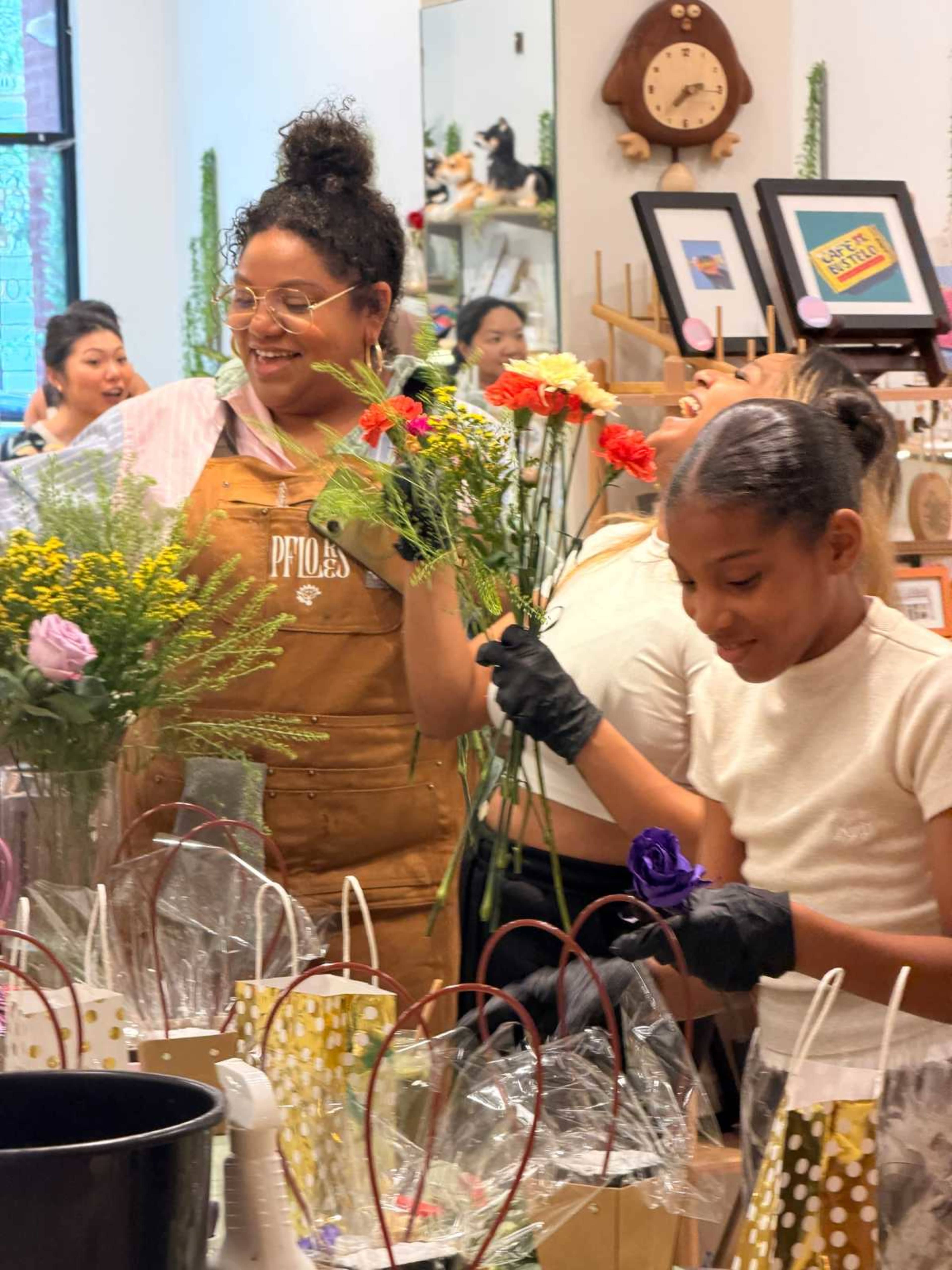 Two women are arranging flowers in a shop filled with plants and decorative items.