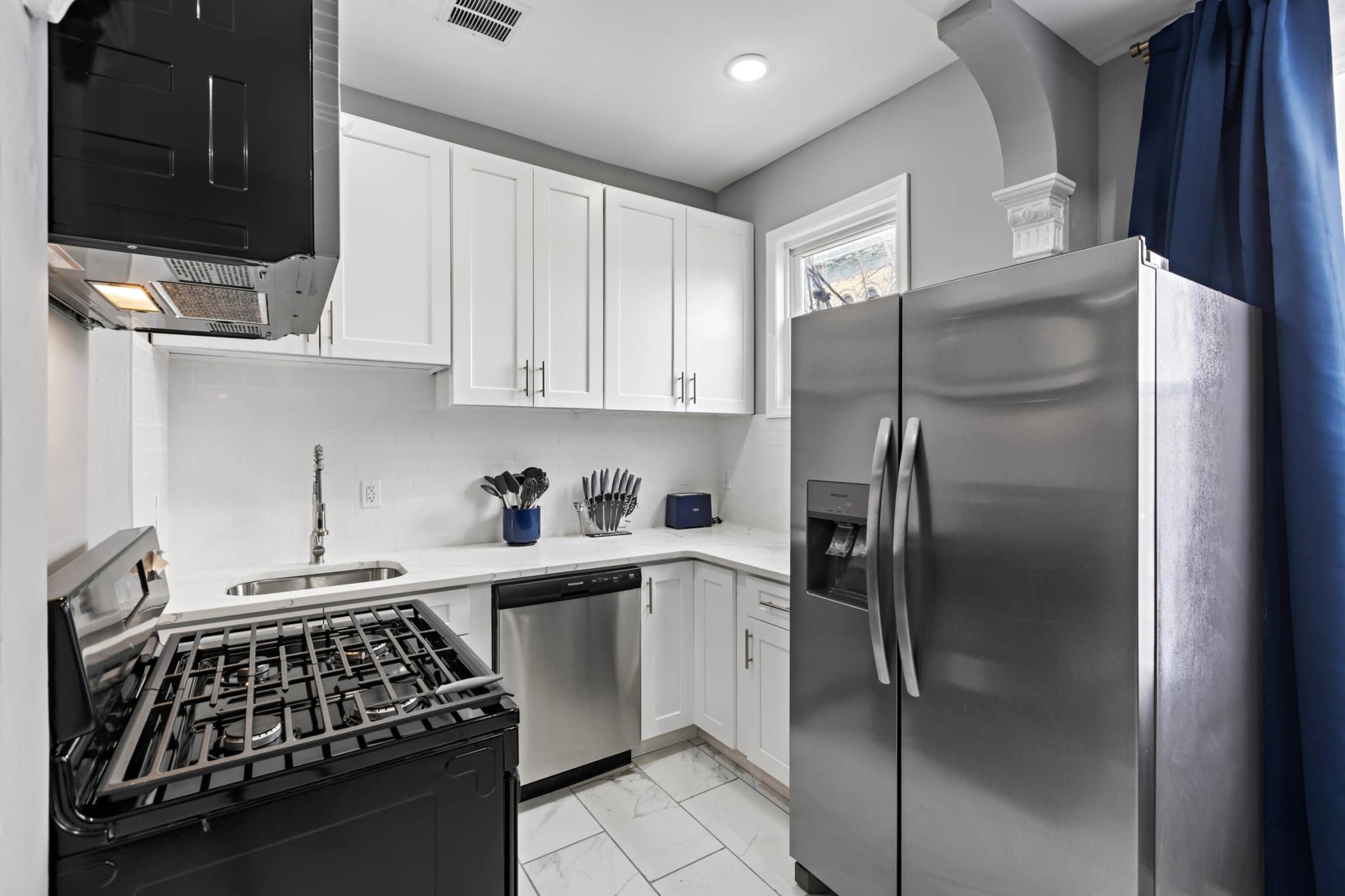 The image shows a modern kitchen with white cabinets, stainless steel appliances, and marble tile flooring.