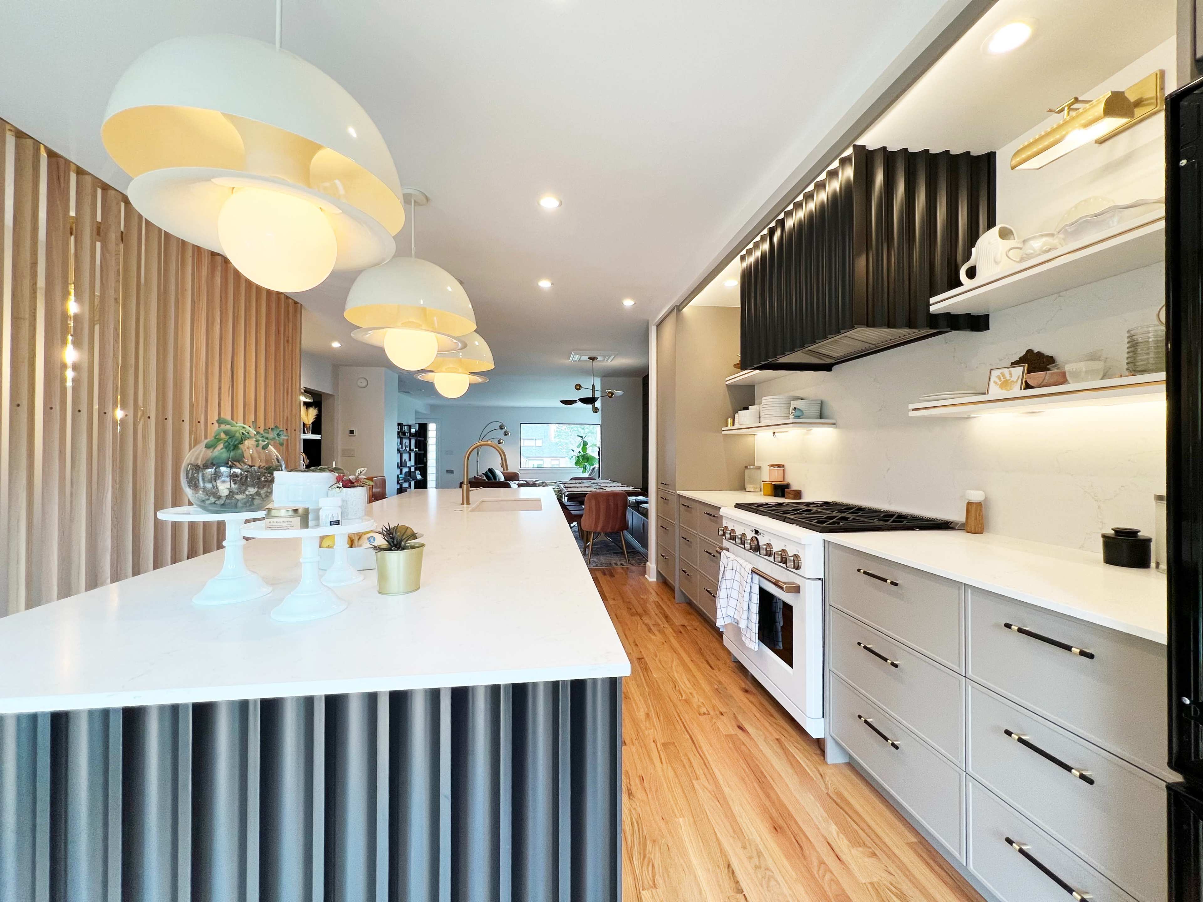 The kitchen features a long white island with ribbed black cabinetry, modern pendant lights, and stainless steel appliances.