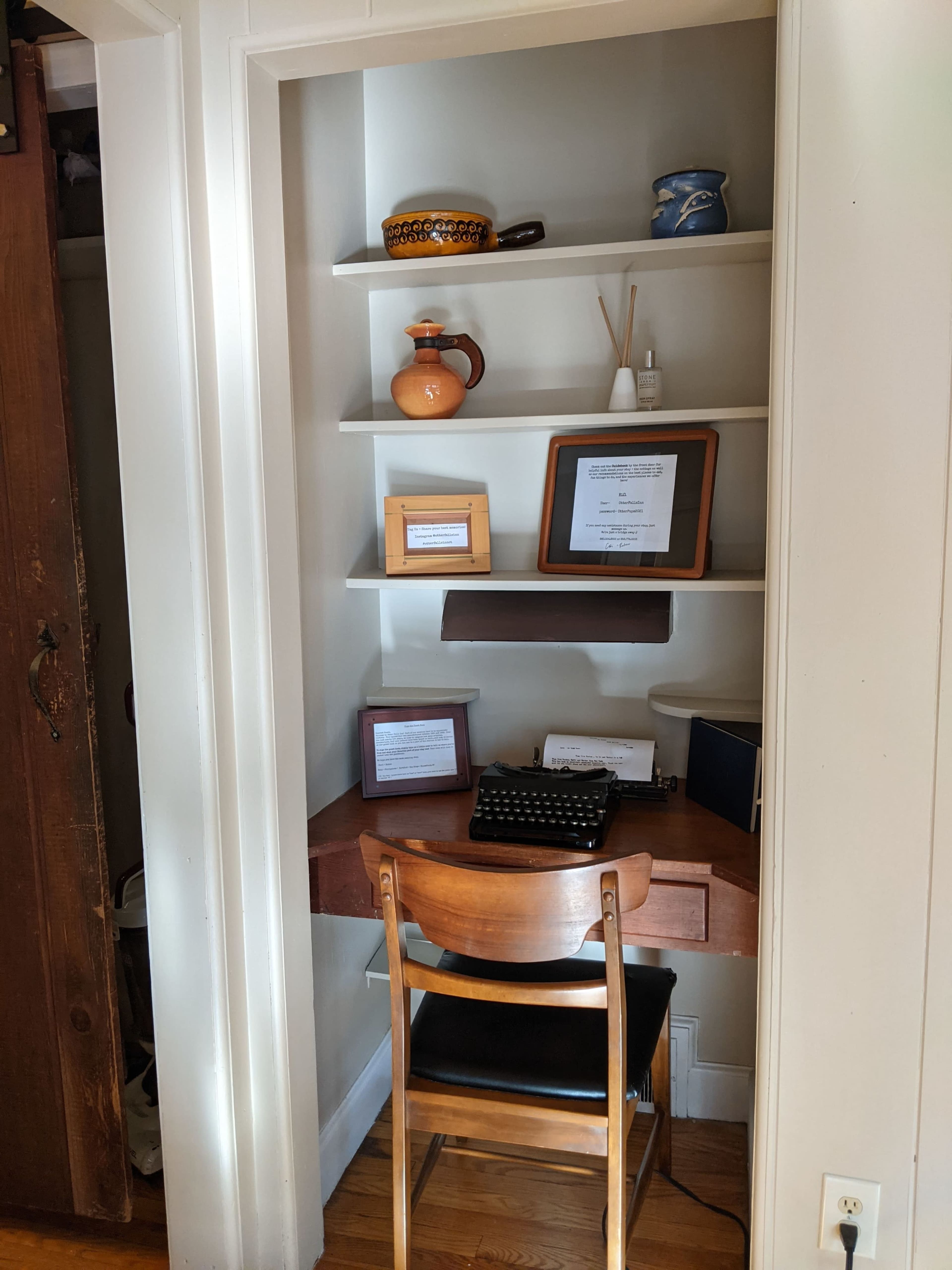 A small nook with shelves displaying decorative items and a wooden desk with a typewriter and framed documents.