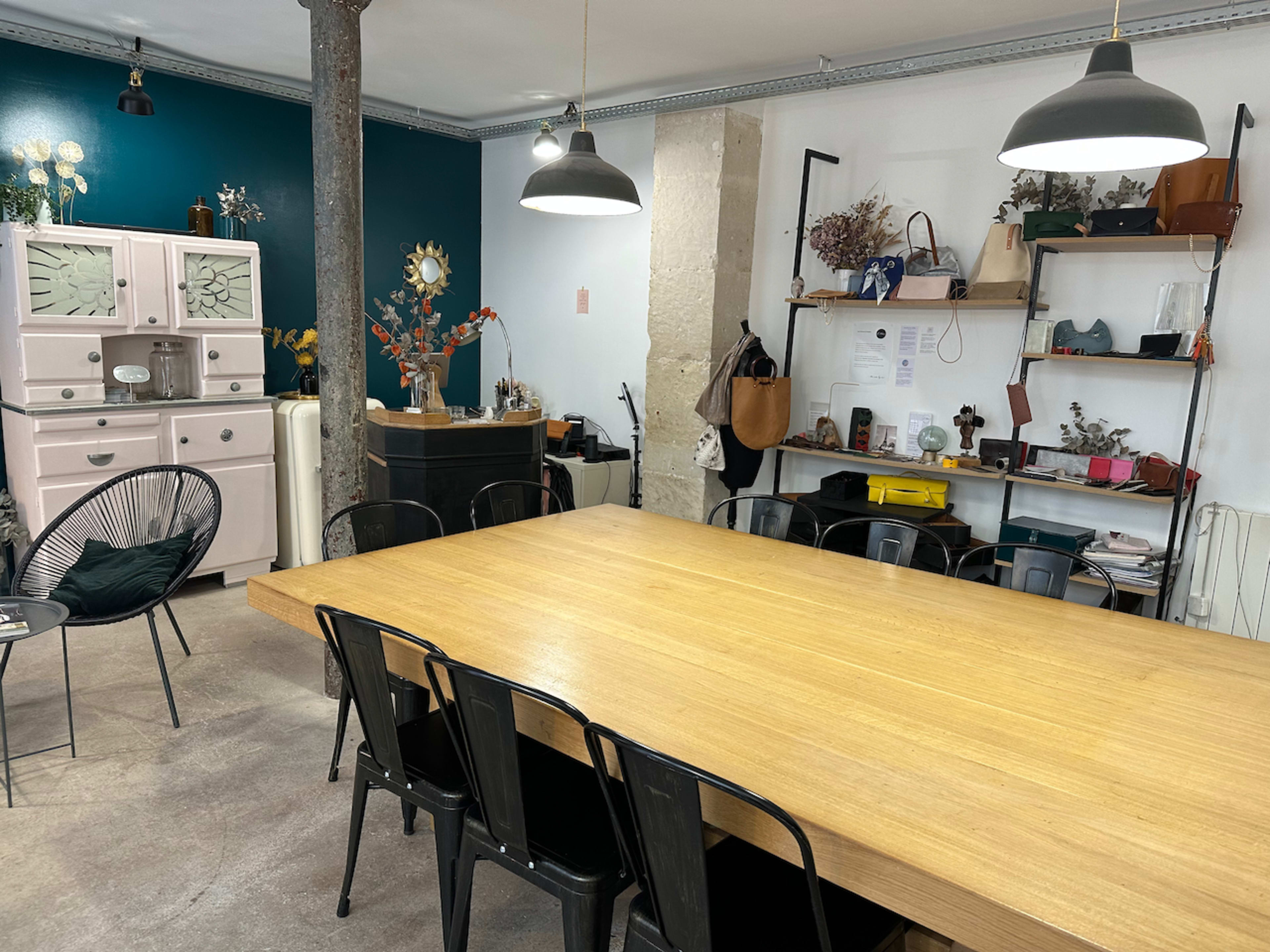 A modern workspace with a large wooden table, black metal chairs, and a section of shelves displaying various items and decor.