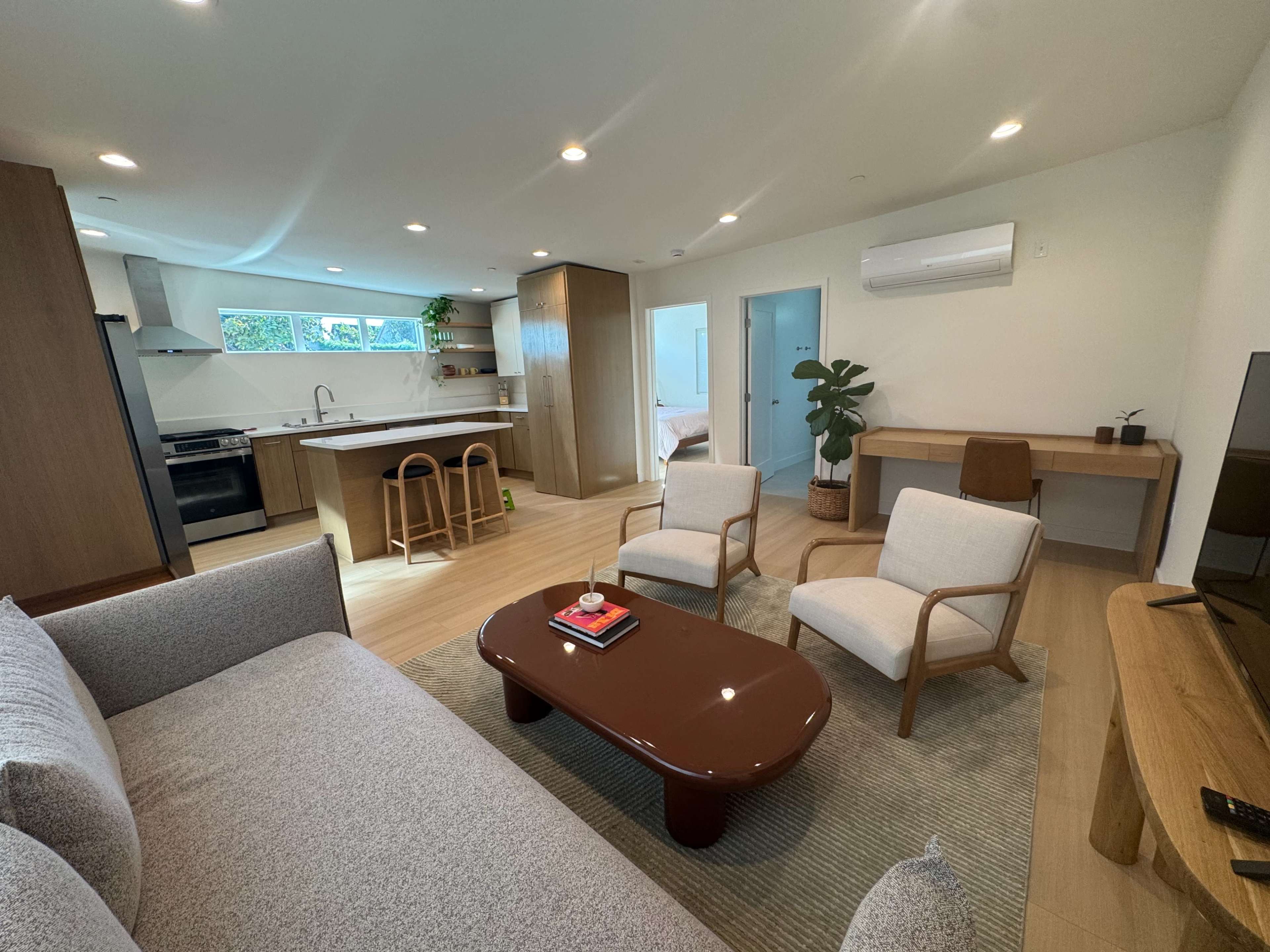 The image shows a modern living room with a sofa, two armchairs, a coffee table, and an open kitchen area in the background.