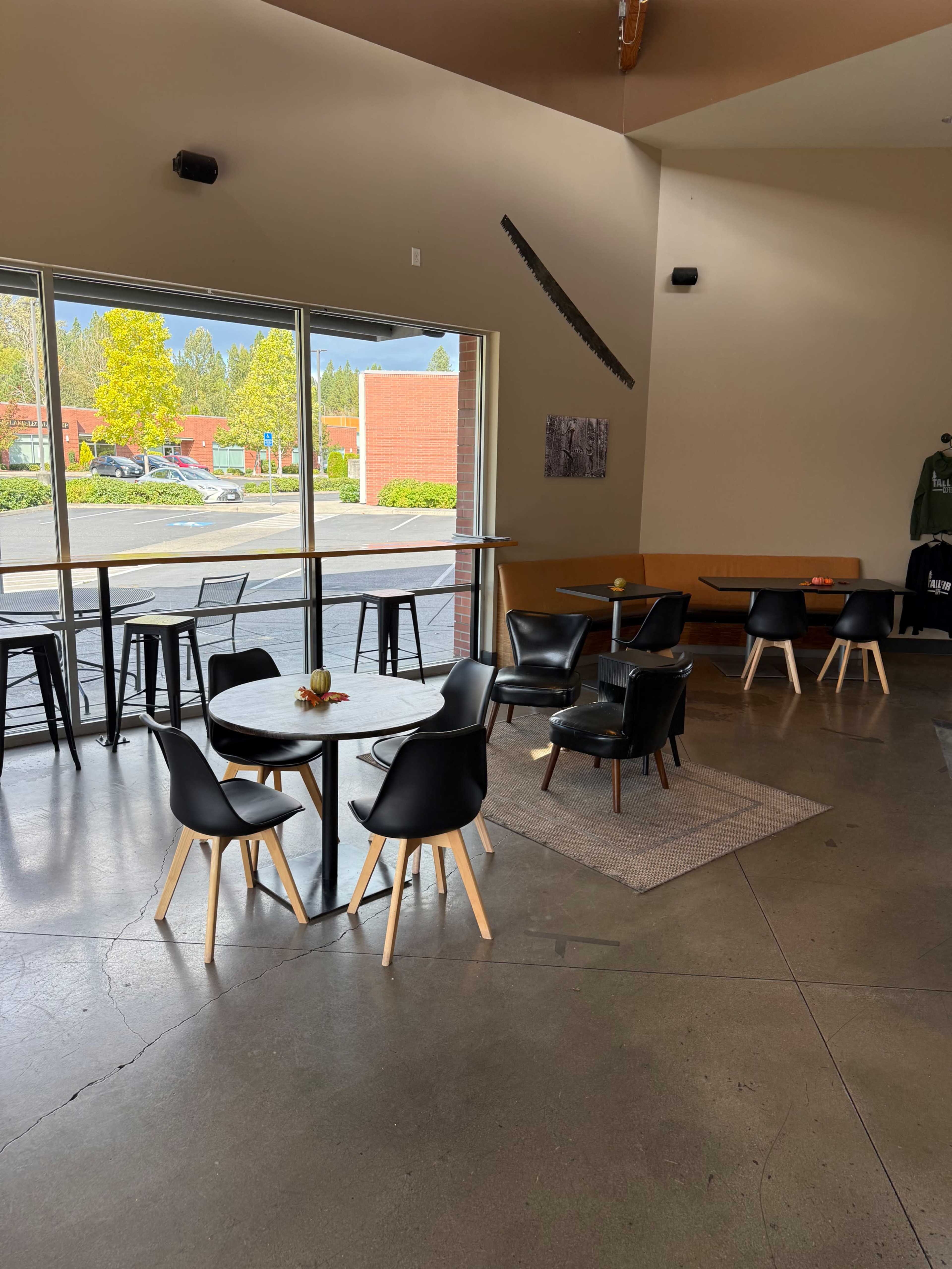 The image shows a modern café interior with black chairs around a circular table, large windows, and a minimalist design.