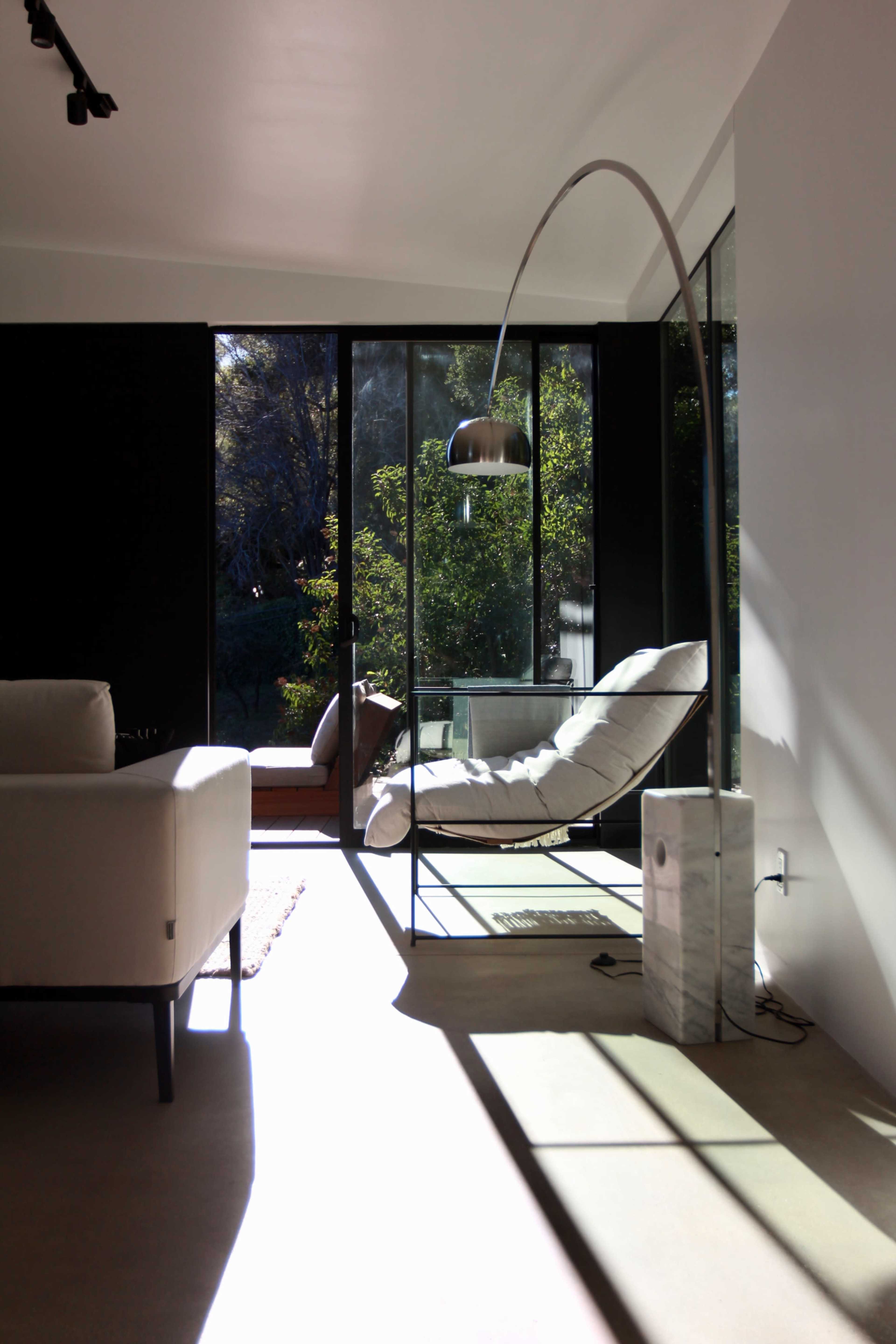 A modern living space with large glass windows, a white couch, and a sleek arc floor lamp beside a chaise lounge.