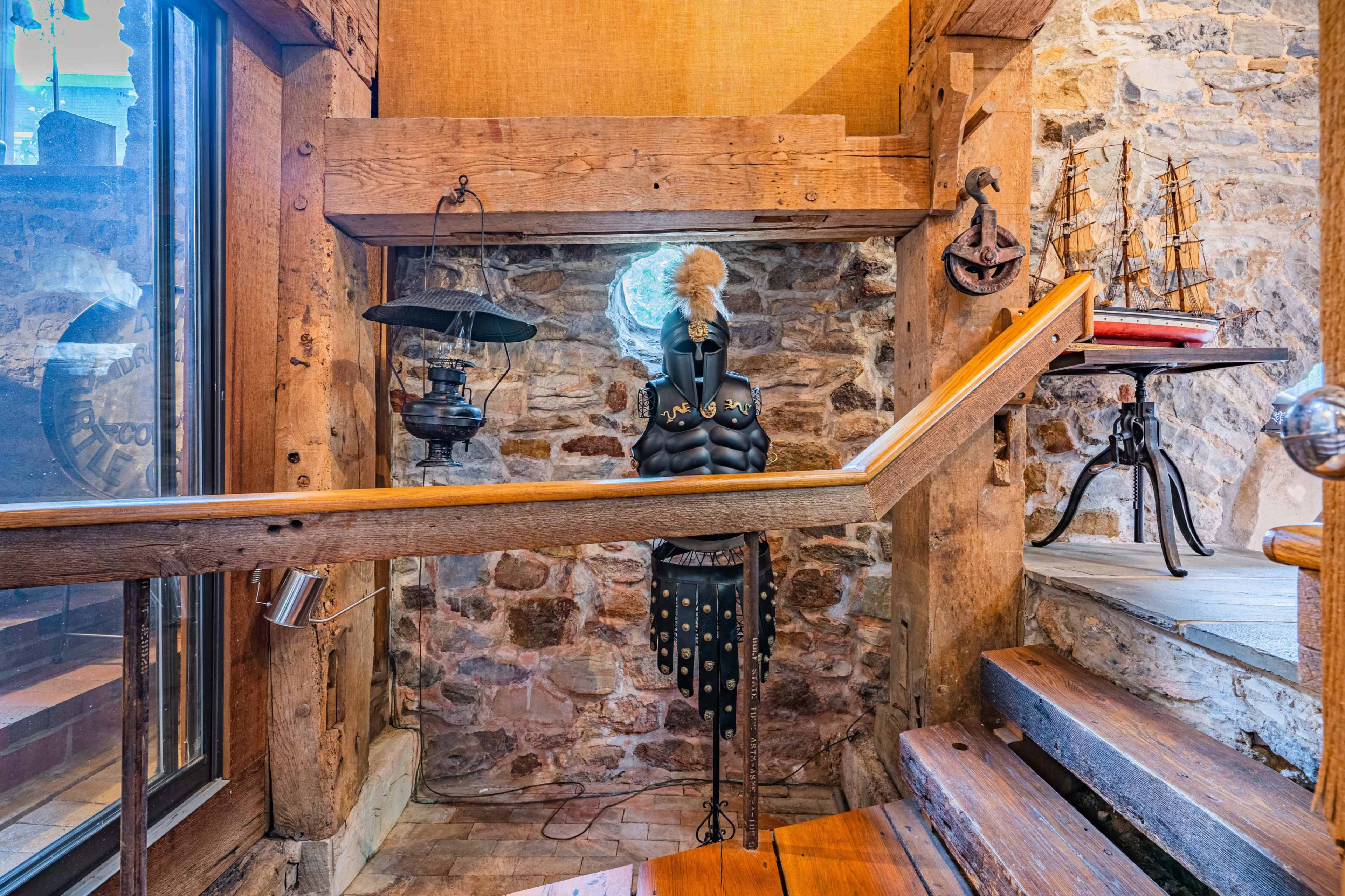 A stairway with wooden steps leading down to a stone wall, featuring a decorative mannequin in armor and a small ship model on a nearby table.