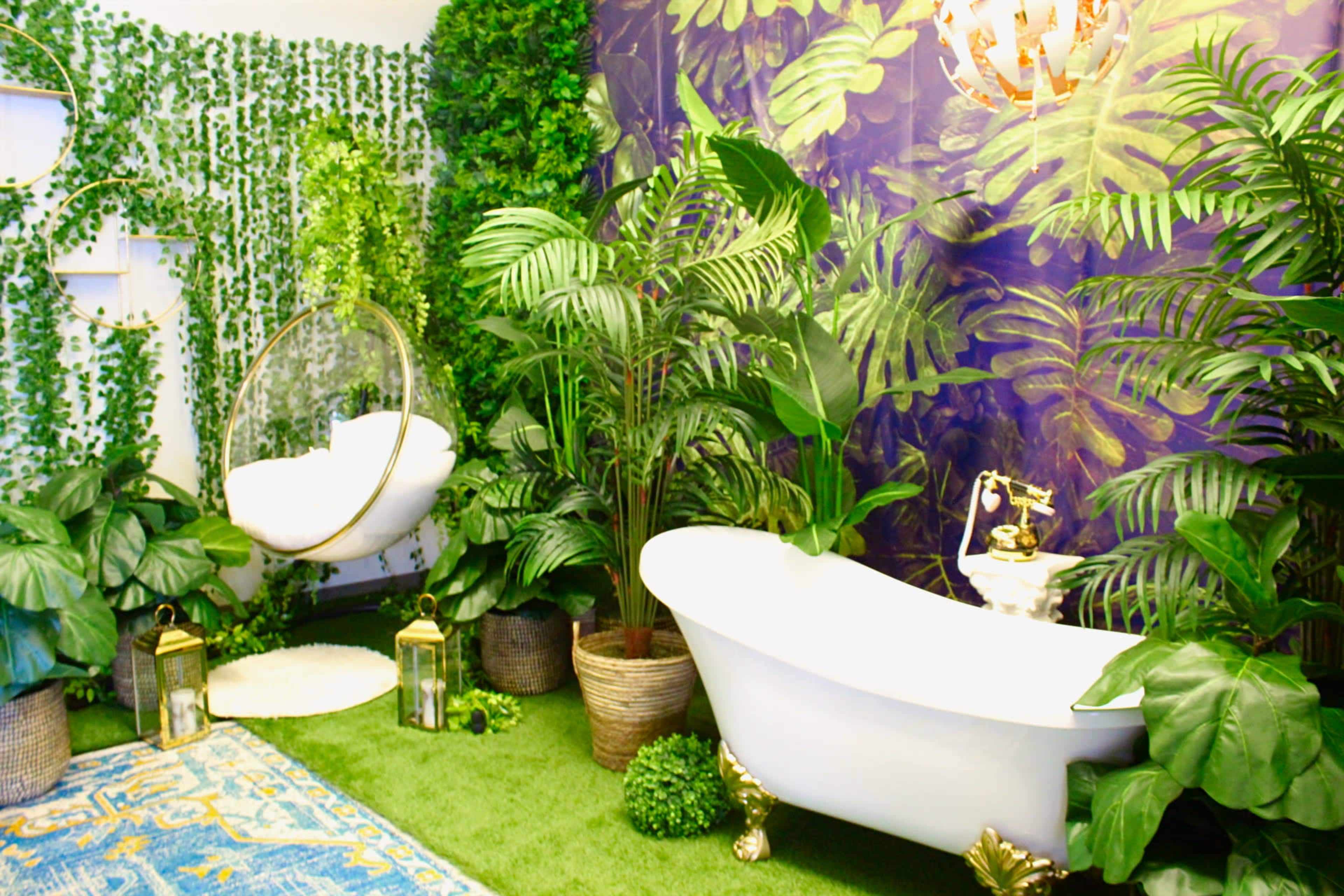 A bathroom decor with a vintage bathtub surrounded by lush greenery, a hanging chair, and decorative plants against a patterned purple wall.