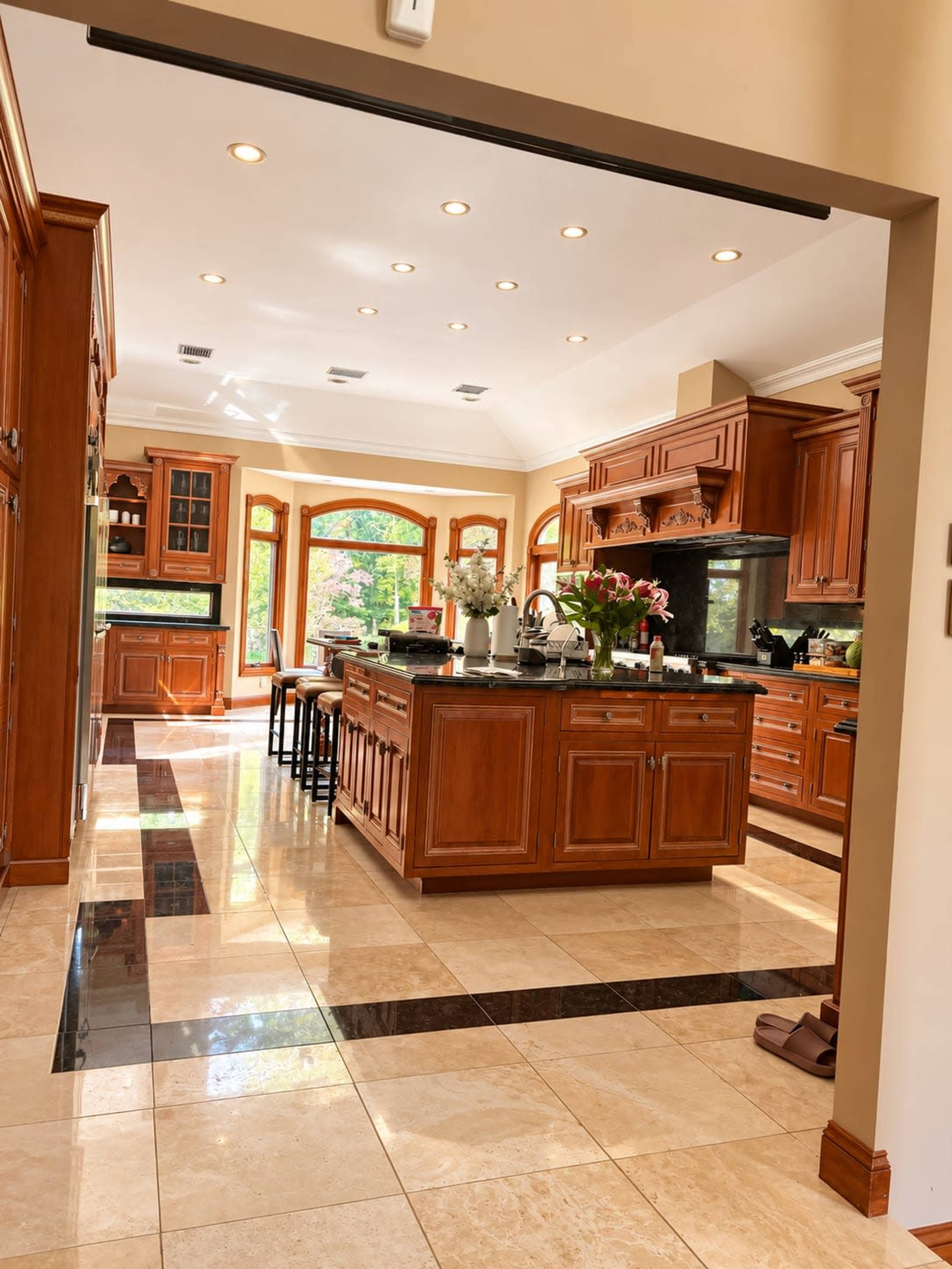 The image shows a spacious kitchen with wooden cabinetry, a central island, and a polished tile floor.