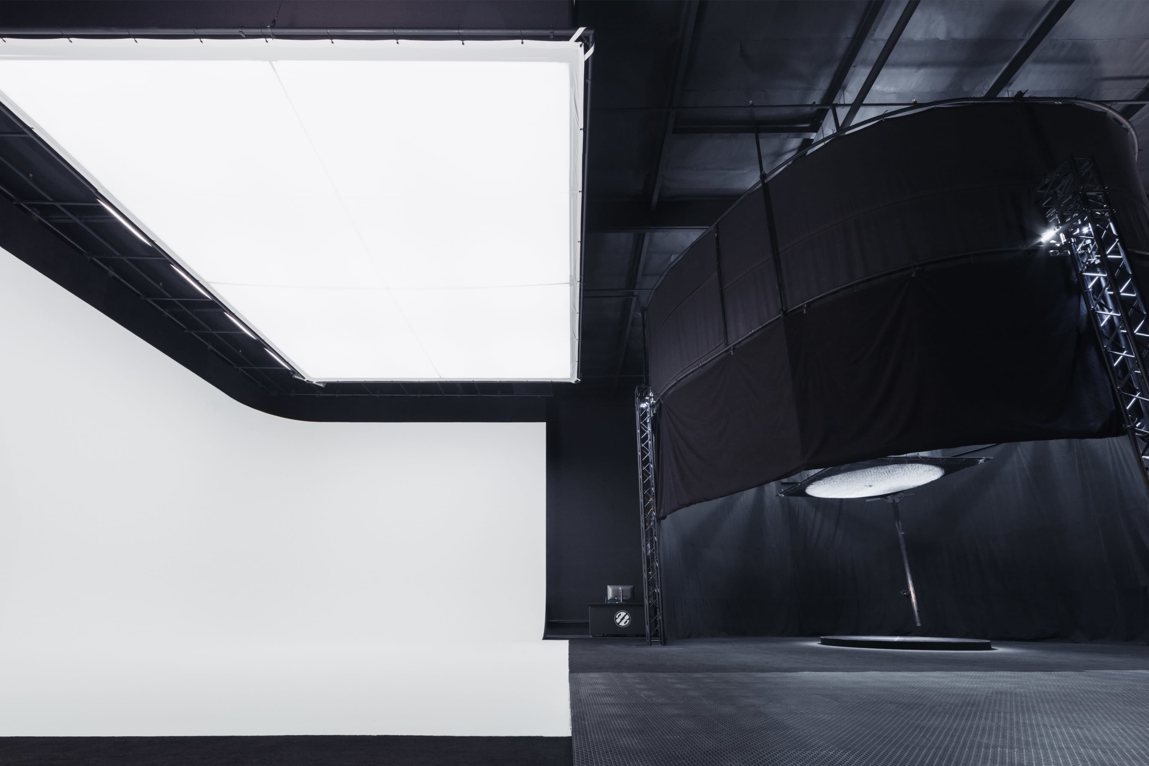 A spacious studio with a large white backdrop on one side and a circular platform enclosed by black fabric on the other.