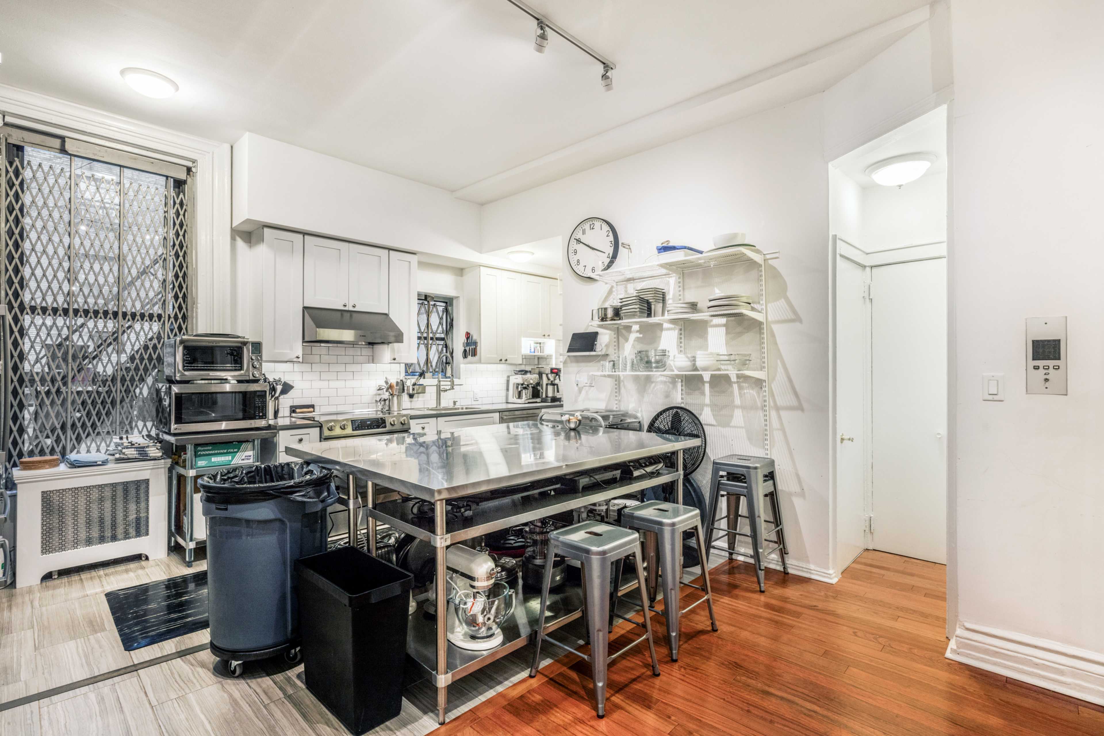 The kitchen features stainless steel appliances, a central island with stools, and white cabinetry against a backdrop of wood and tile flooring.