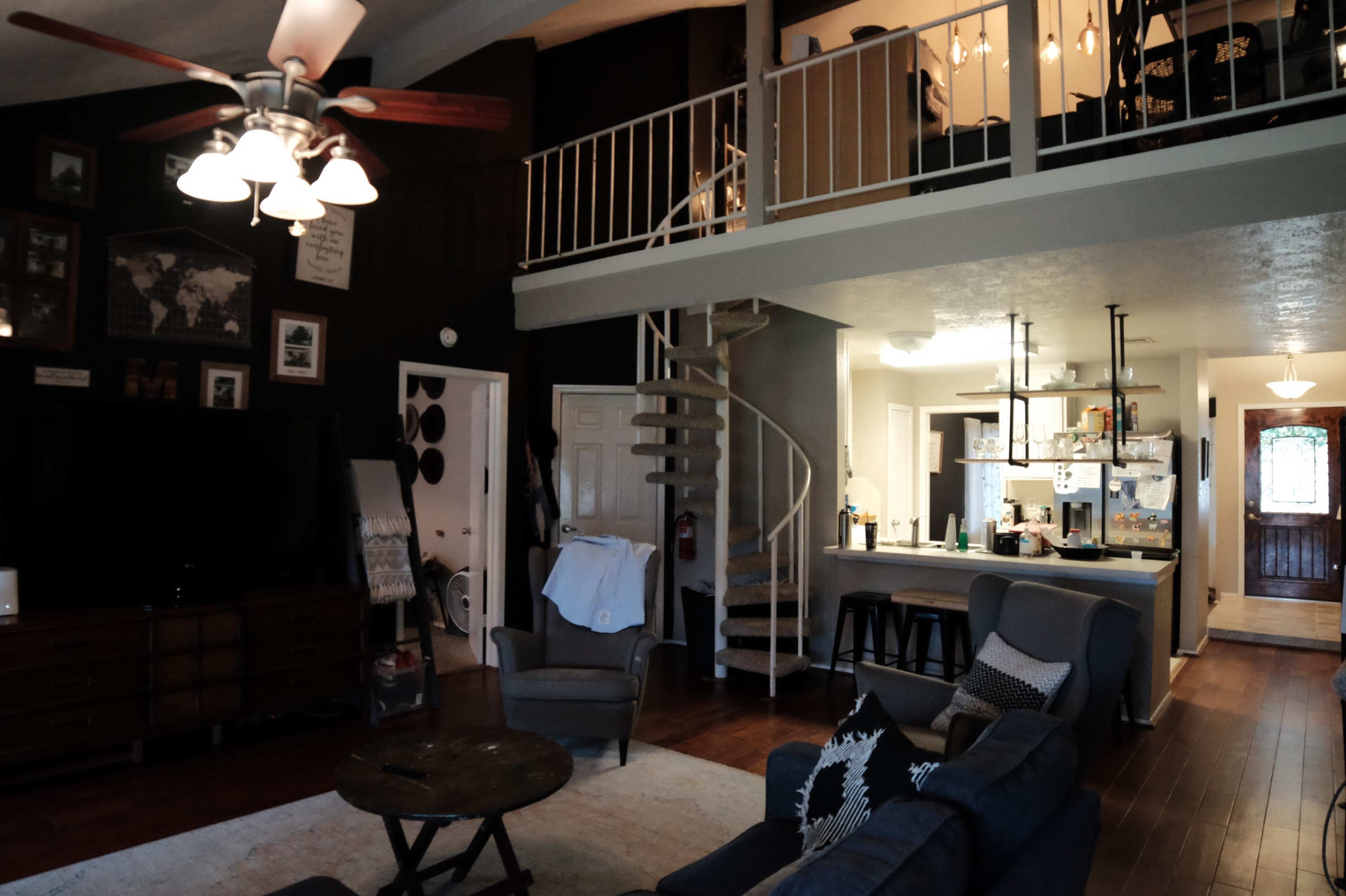 A modern living room with a spiral staircase leading to an upper level, featuring a kitchen area and a door leading outside.