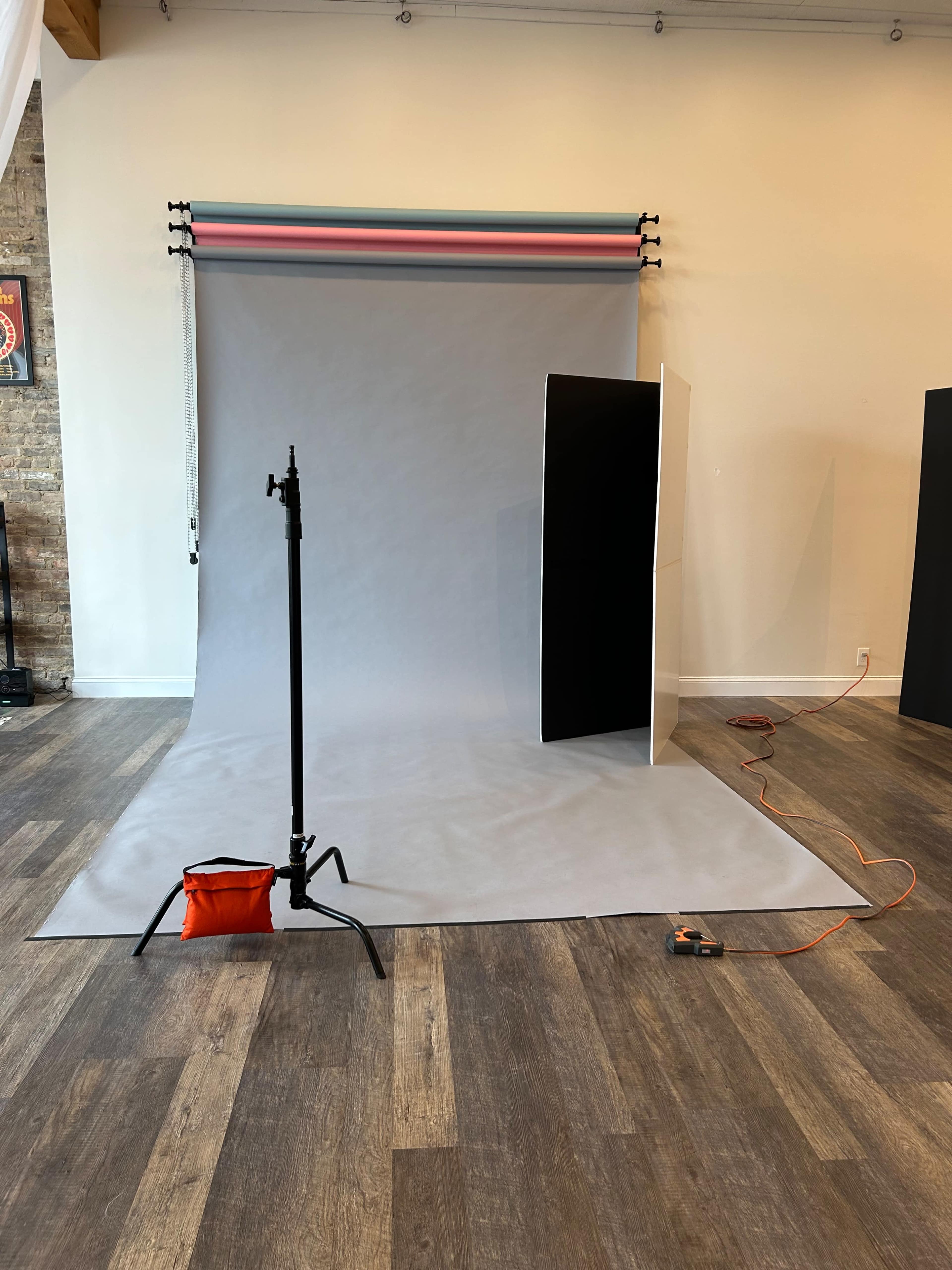 The image shows a photography studio setup with a gray backdrop, a light stand, and props arranged on the floor.