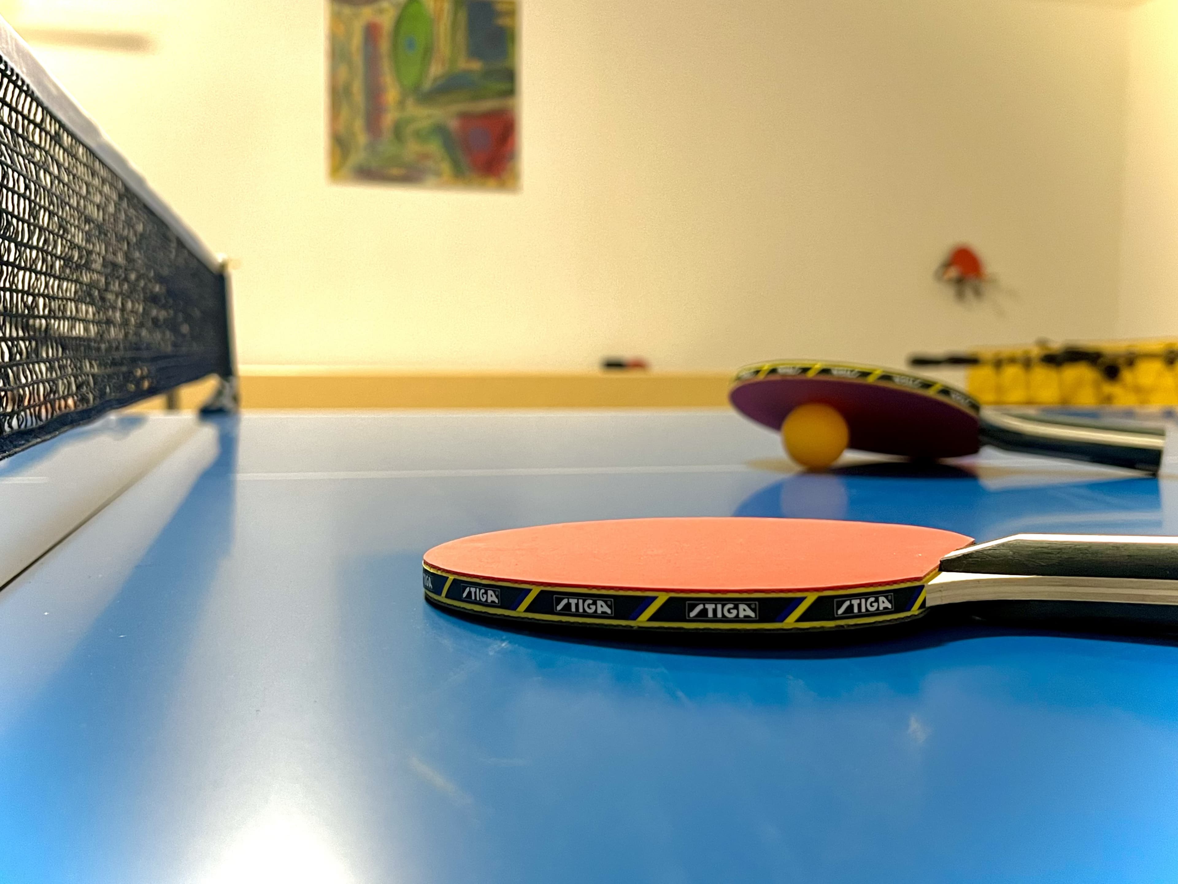 A close-up of table tennis paddles and a ball resting on a blue table in a recreational space.
