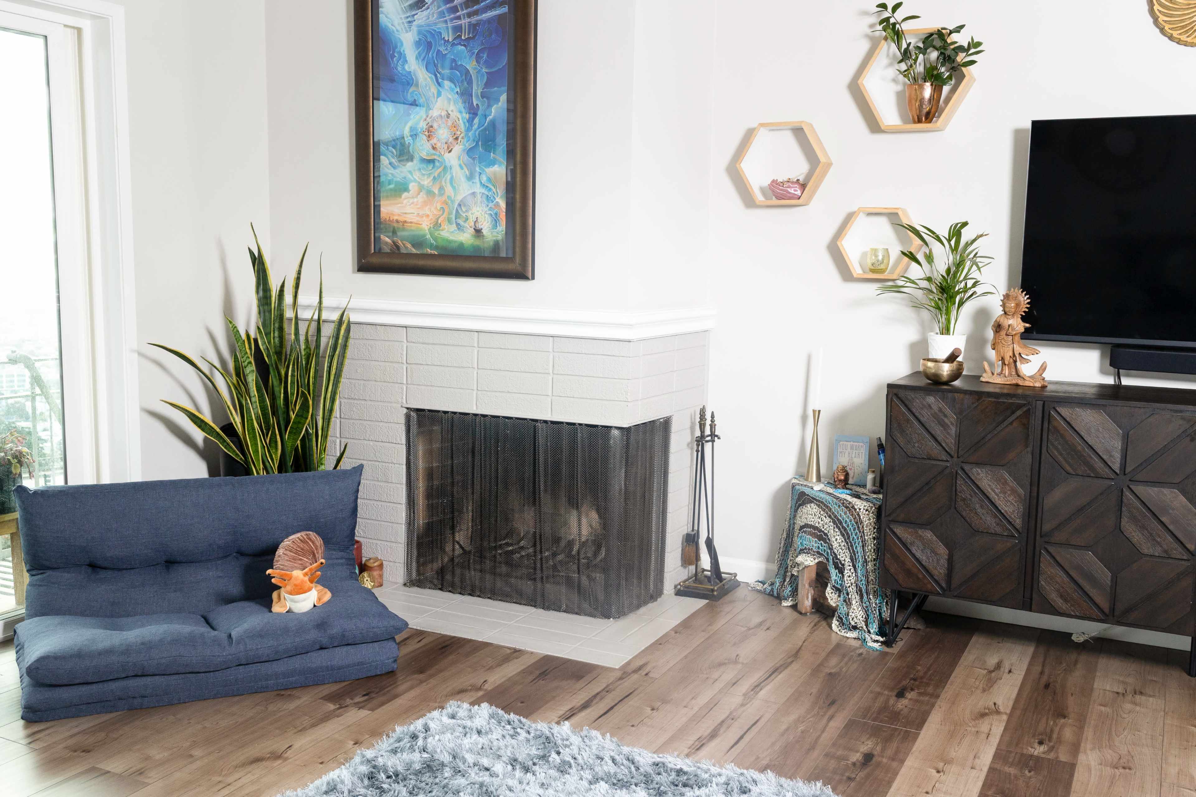 The image depicts a modern living room with a blue couch, a fireplace, a wooden TV stand, and decorative plants on the walls.