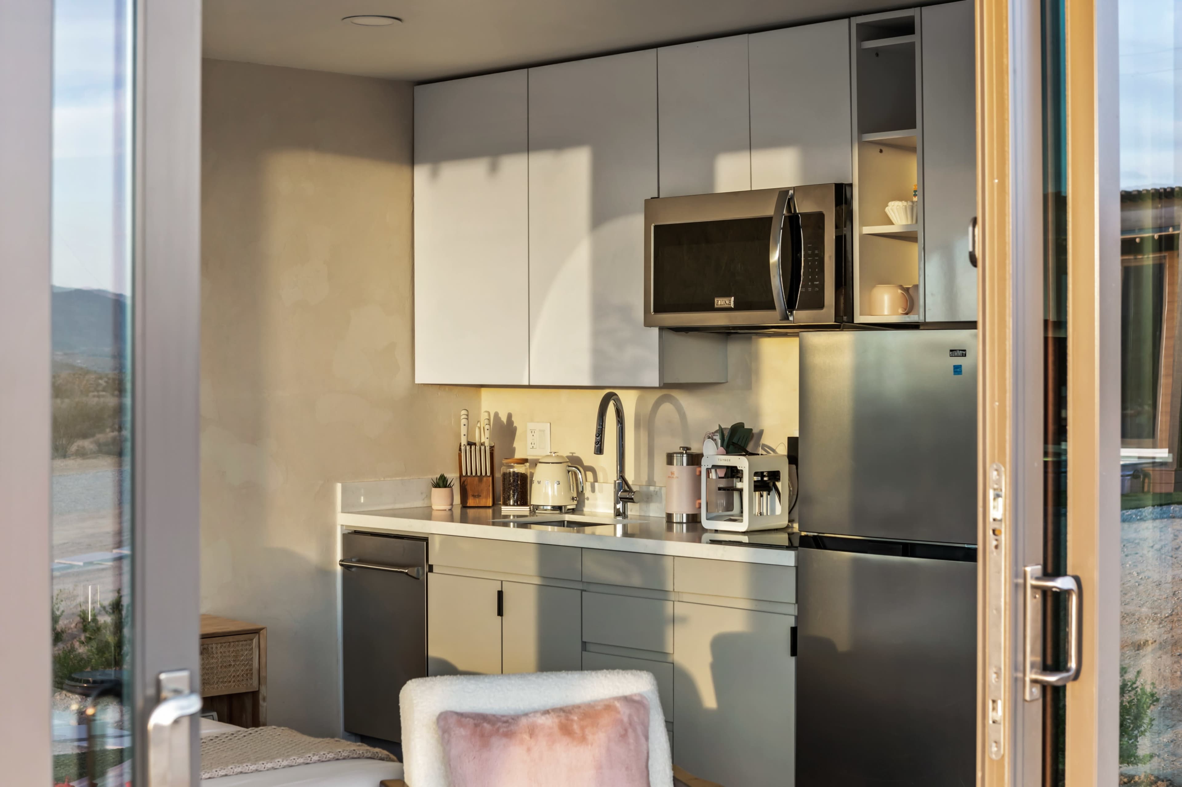 The image shows a modern kitchen with white cabinets, stainless steel appliances, and a breakfast bar, illuminated by natural light.