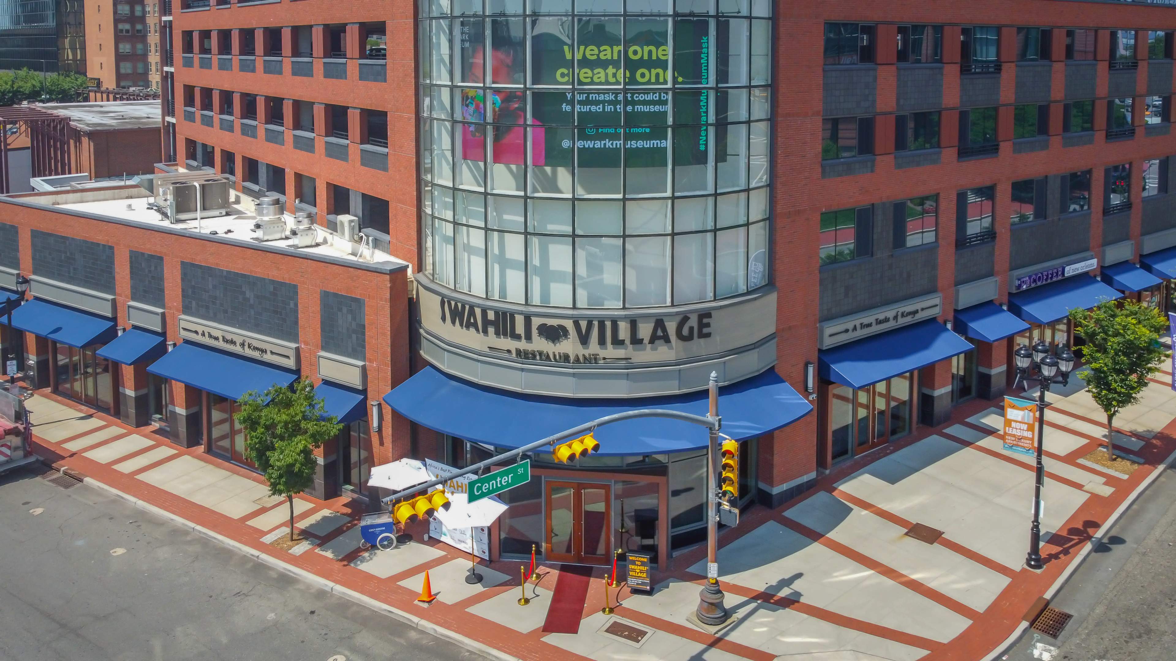 A restaurant named "Wahili Village" located in a modern brick building on a street corner, with blue awnings and a large advertisement in a window.