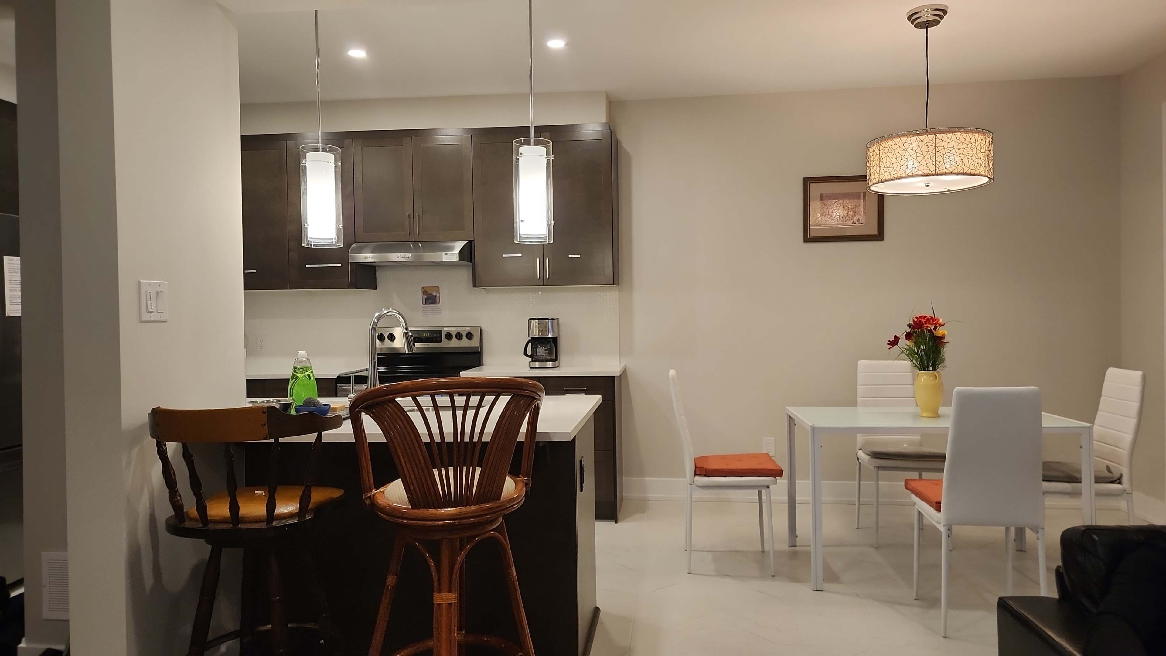 A modern kitchen and dining area with dark cabinetry, a table for four, and bar seating.