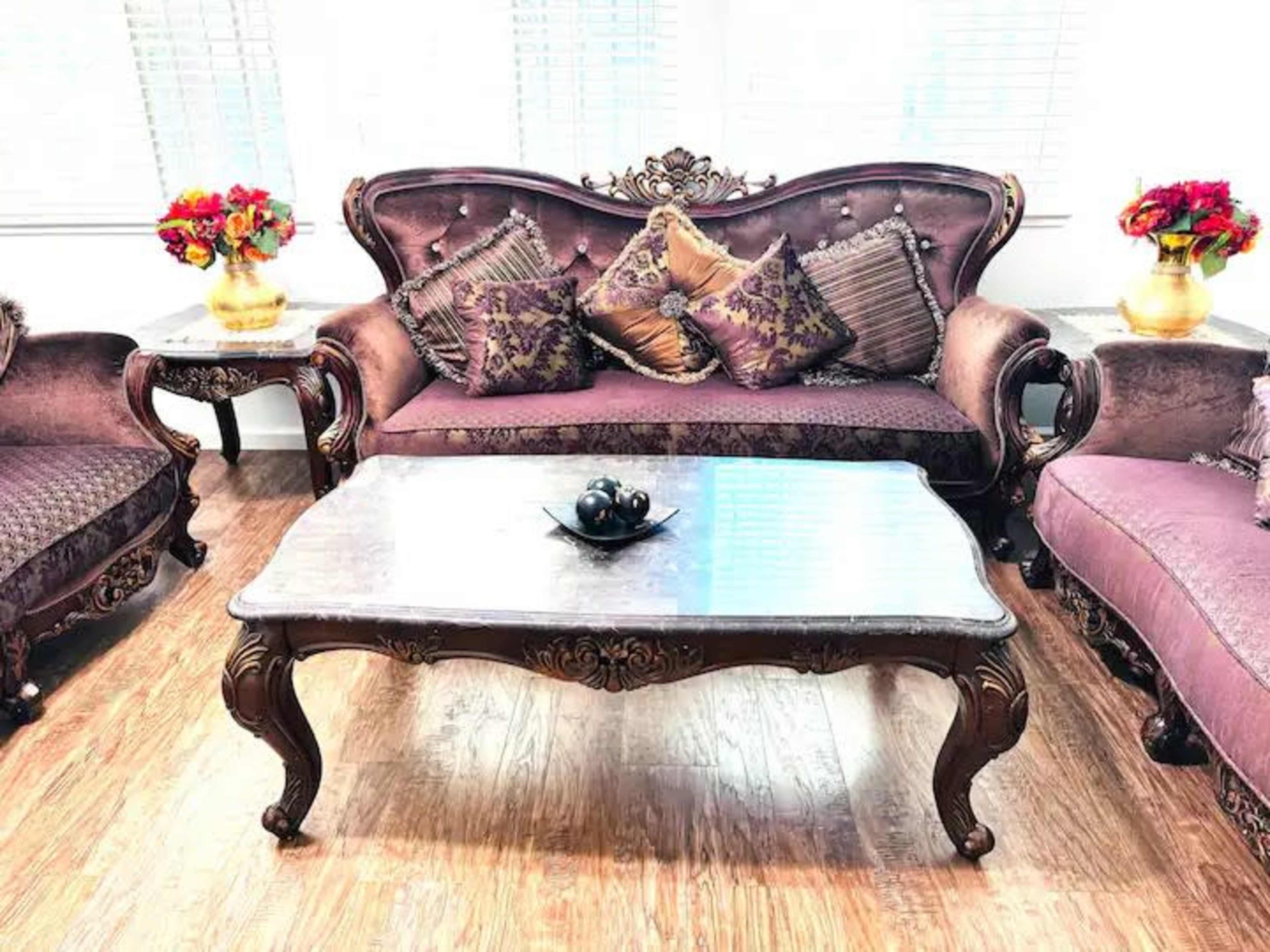An elegantly furnished living room featuring a purple velvet sofa, matching chairs, and a marble coffee table with decorative items.