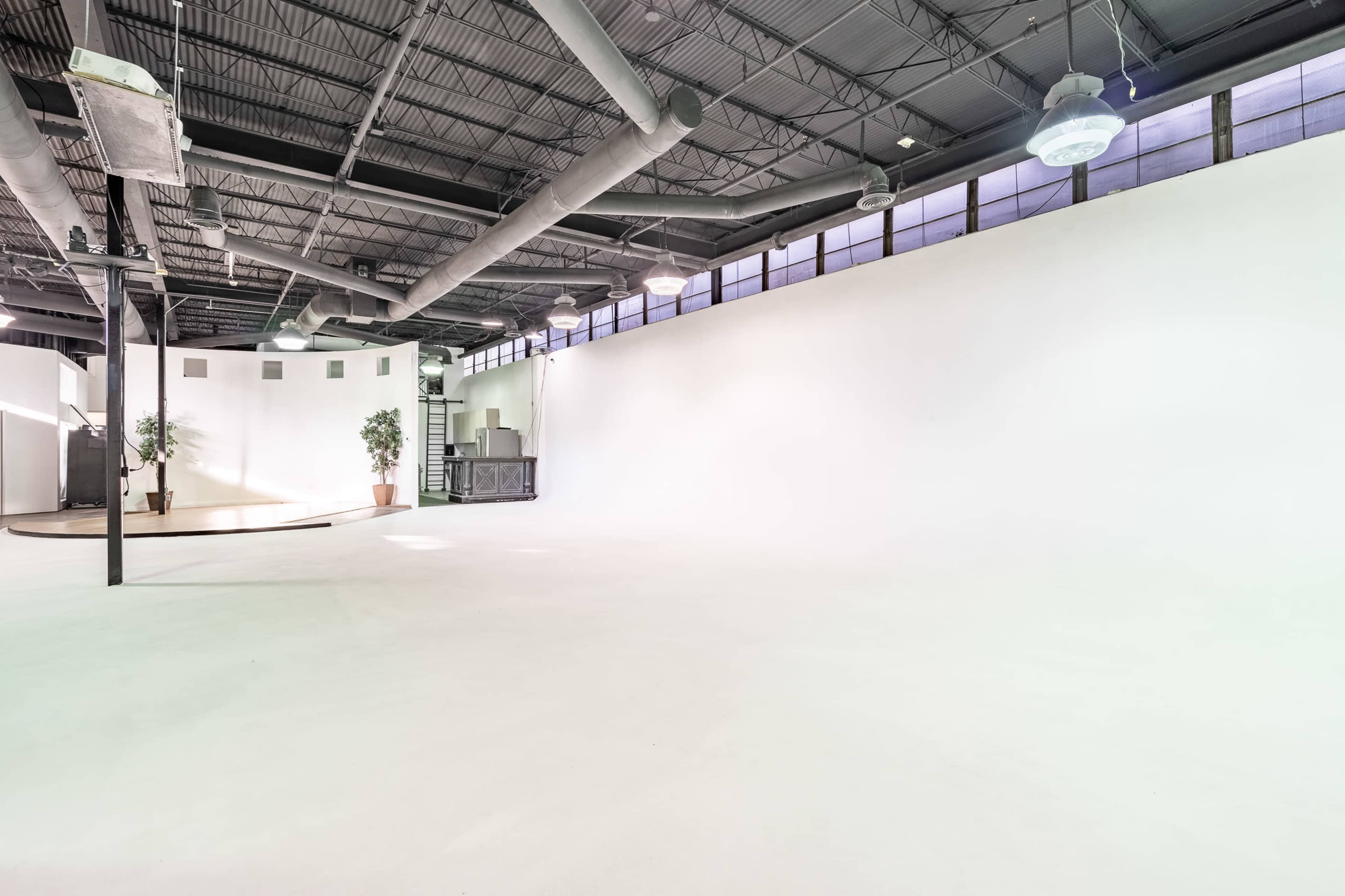 A spacious, empty interior with a high ceiling, concrete floor, and large windows.